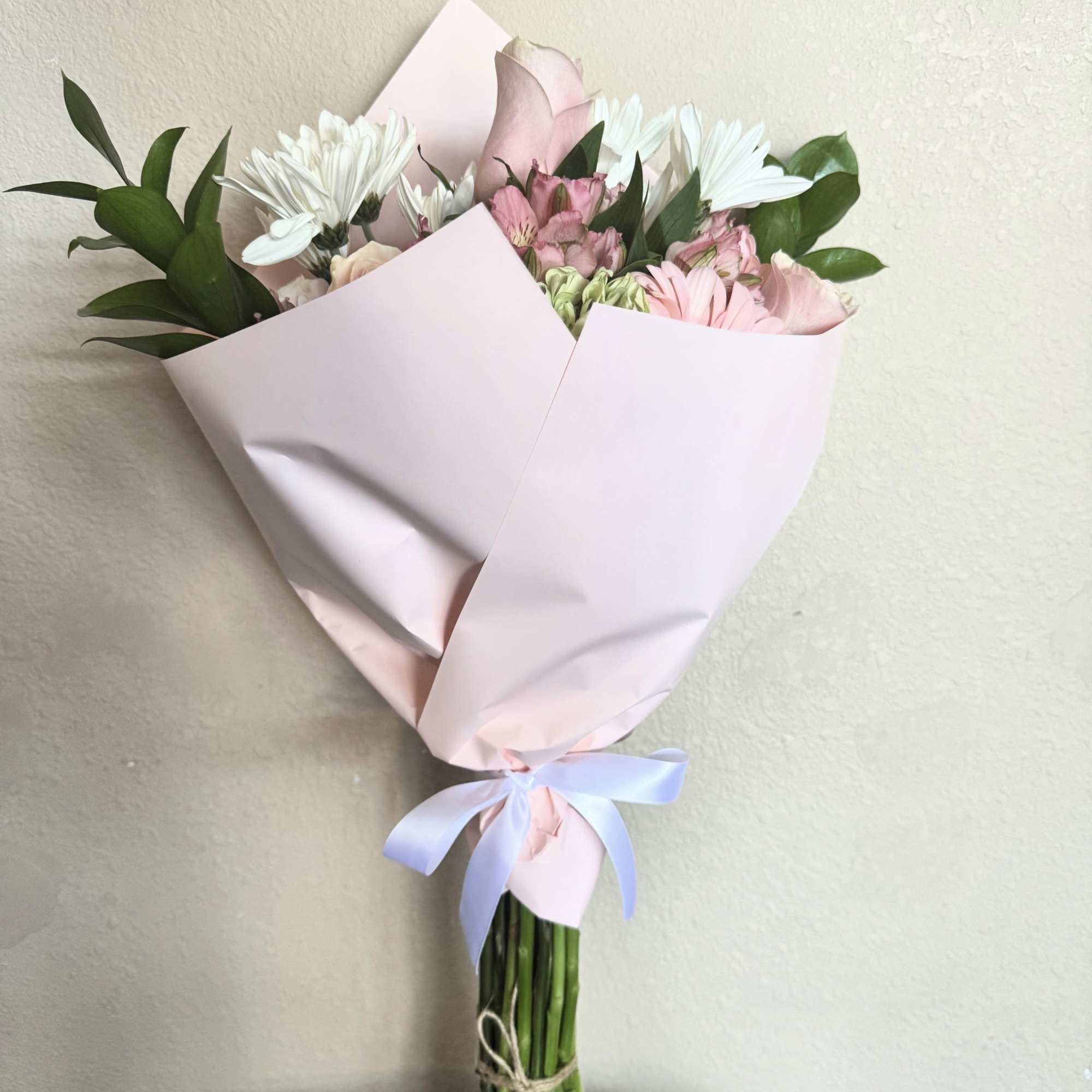 Pink and white mixed bouquet wrapped in pale pink paper with a ribbon.