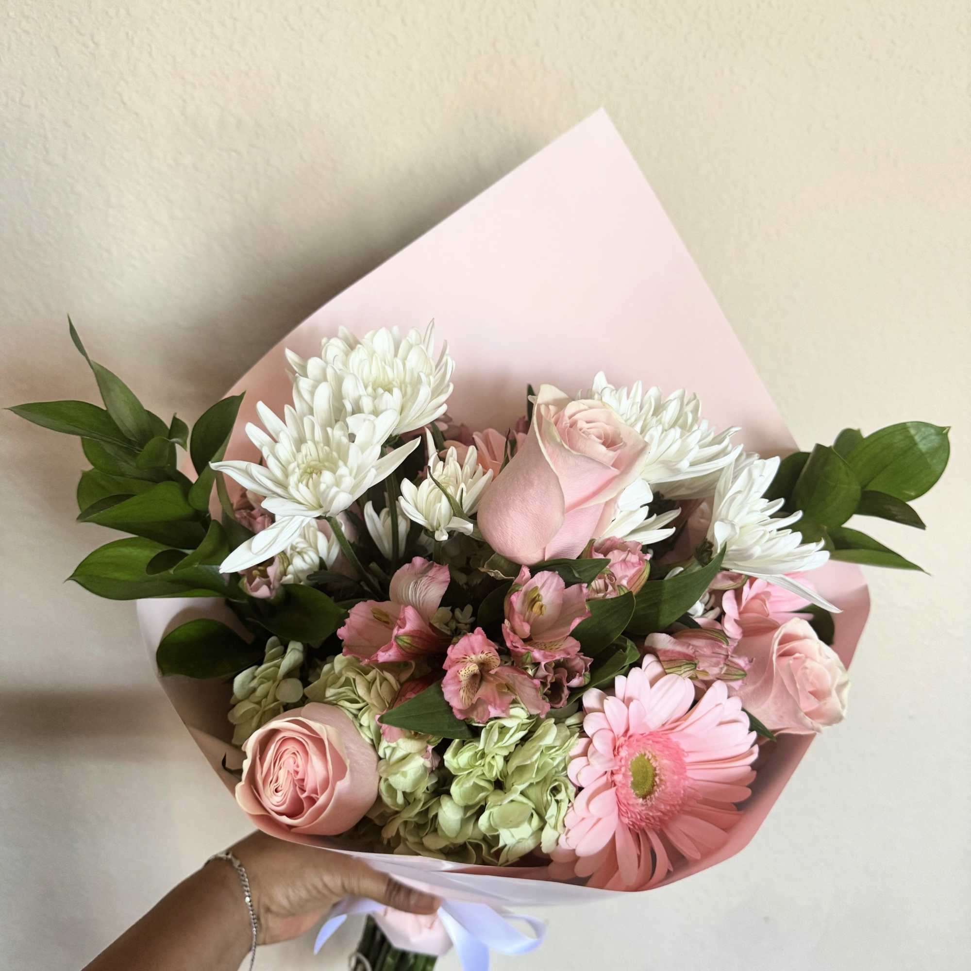 Pink and white bouquet with roses, daisies, and hydrangeas wrapped in pastel paper