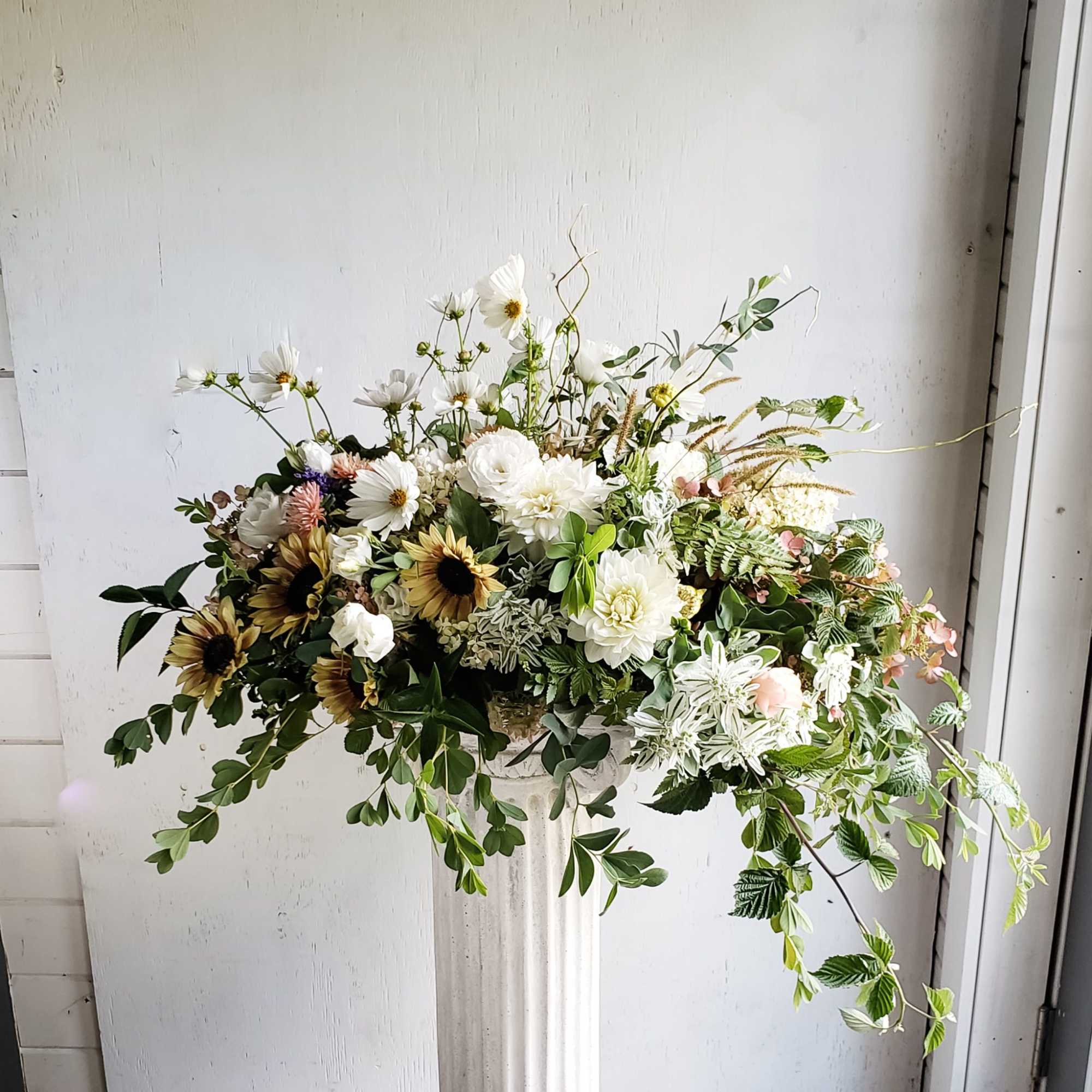 Large white floral arrangement in a tall pedestal vase