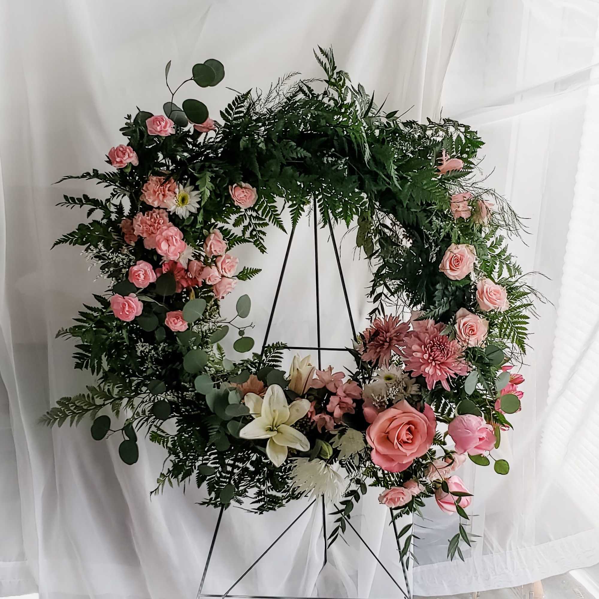 Pink and white floral wreath on a black stand