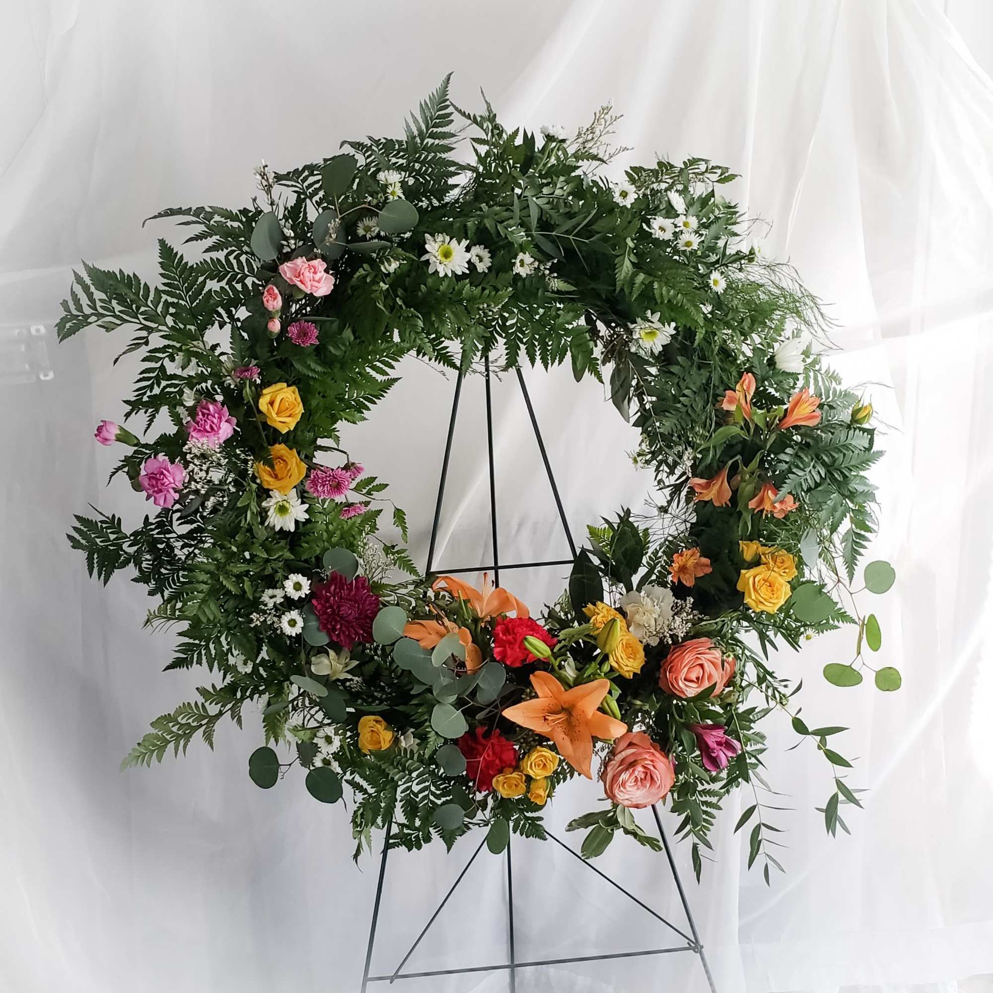 Large floral wreath on a metal stand with mixed blooms and greenery