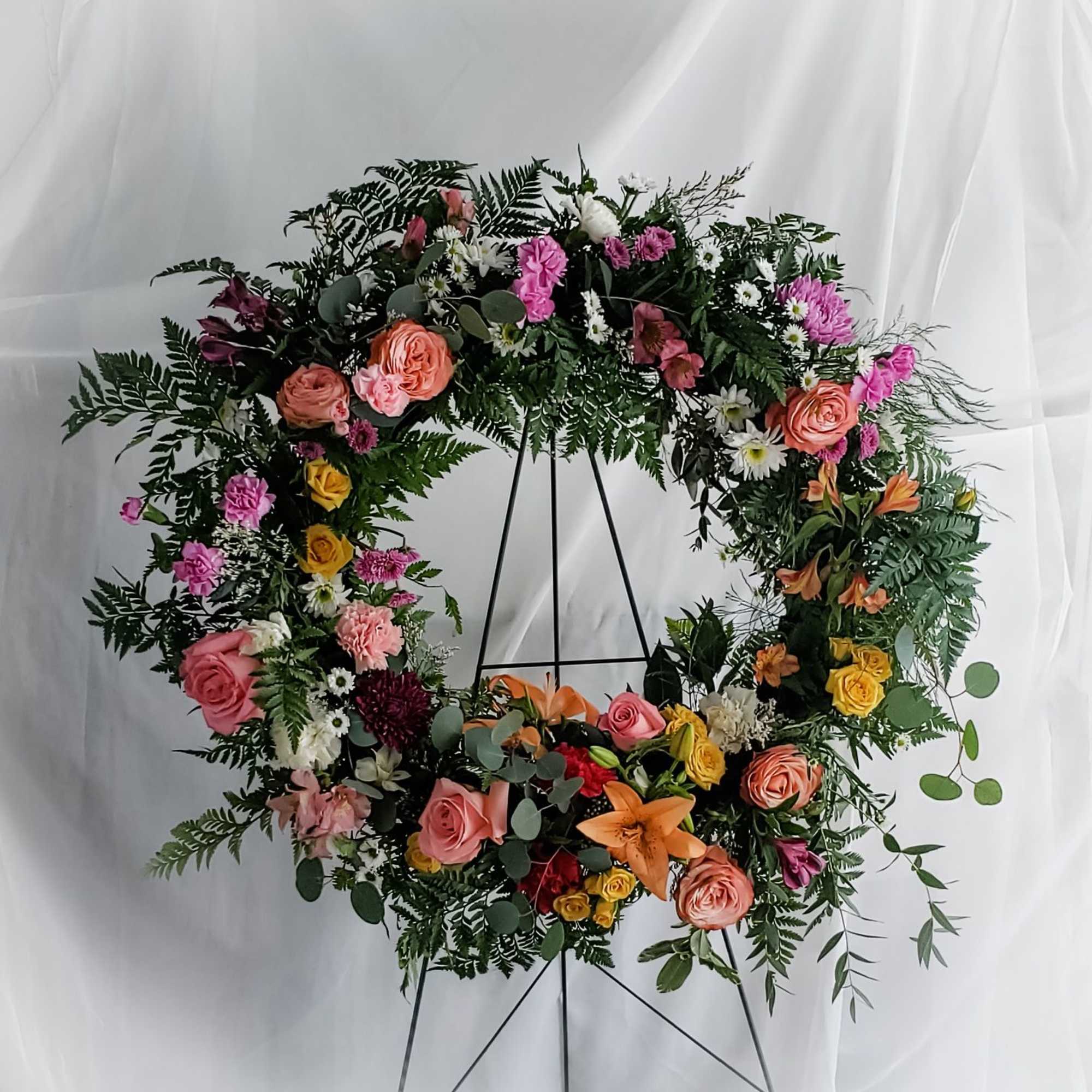 Large floral wreath with pink, orange, and yellow blooms on a black stand