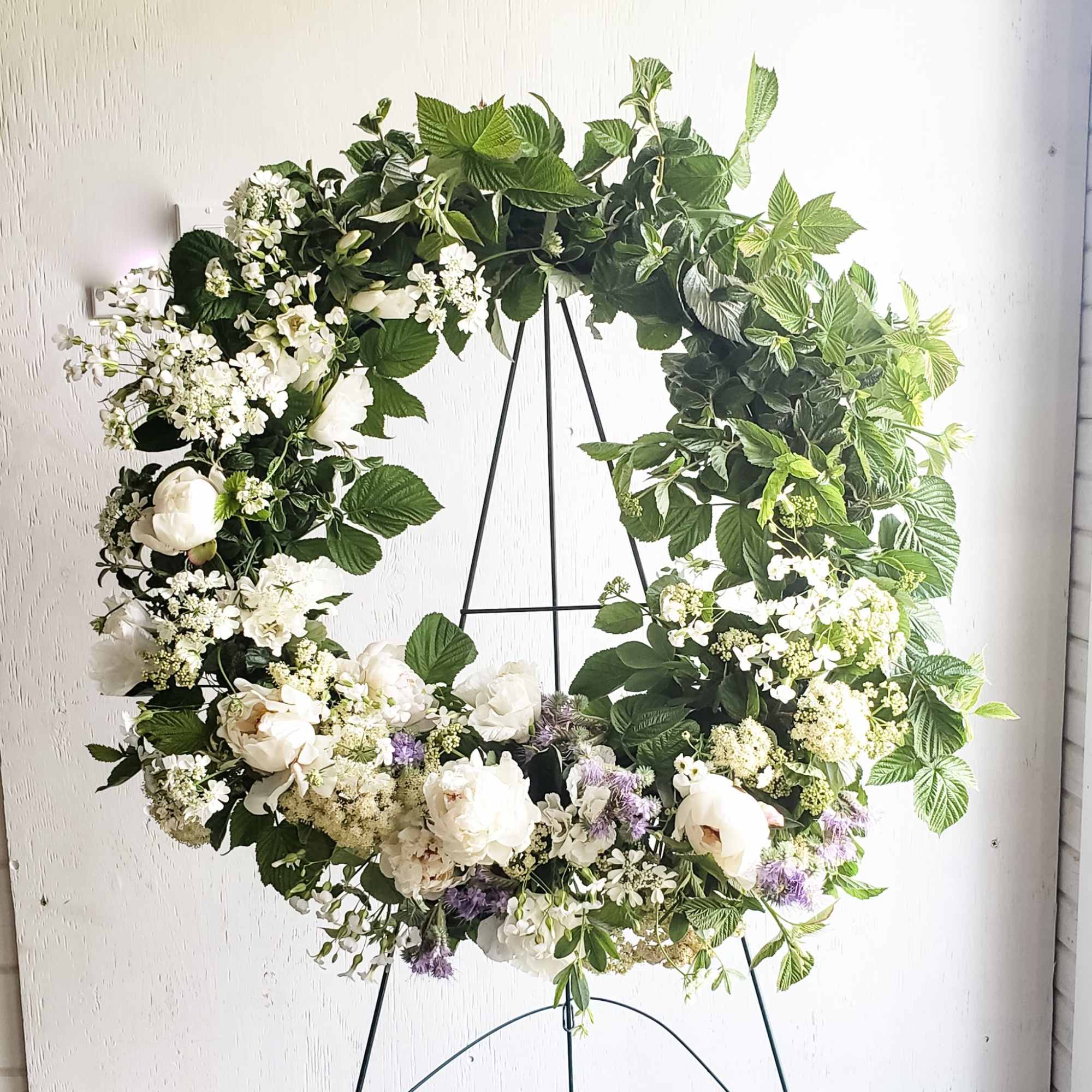 Large floral wreath with white blooms and green foliage on a black stand