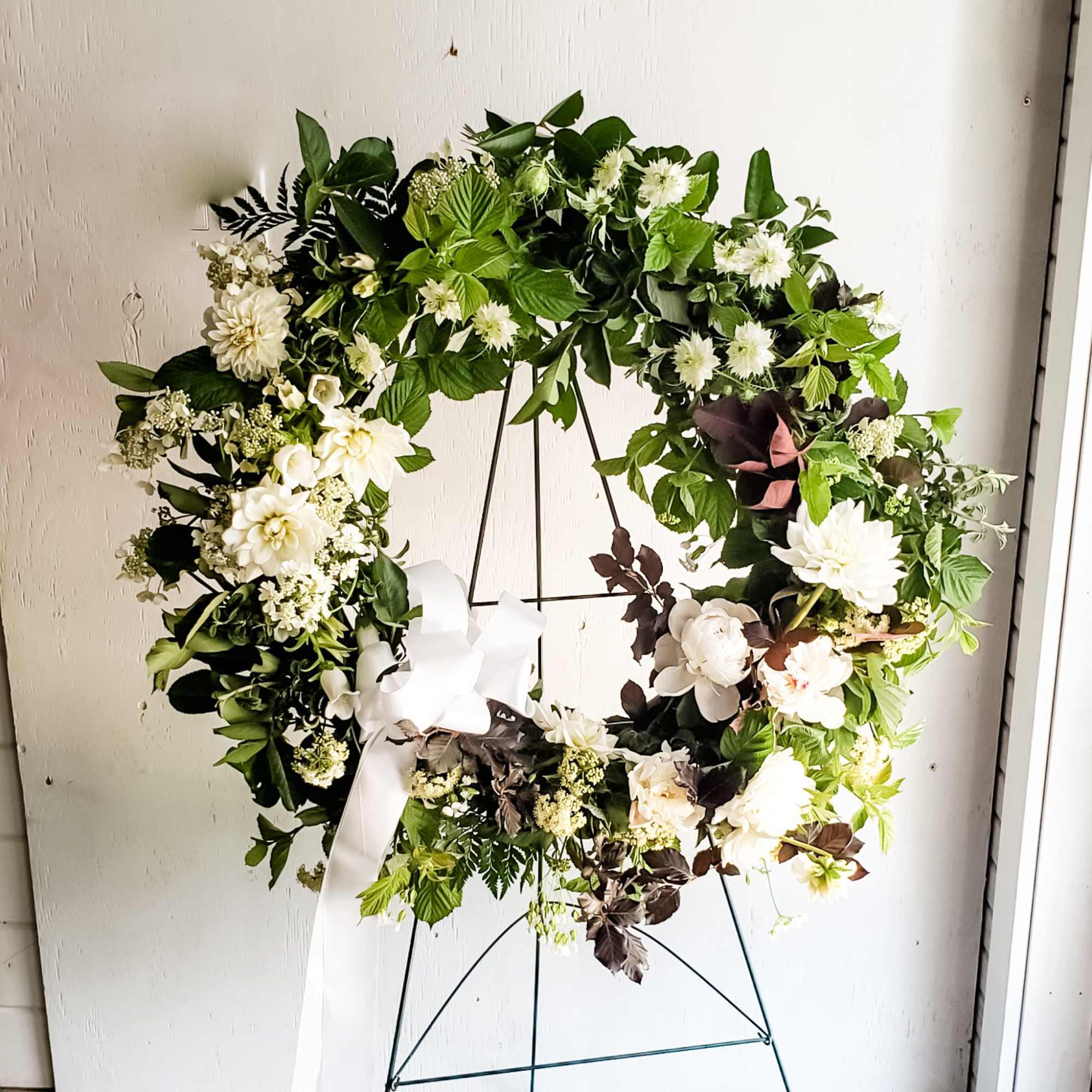 Large white floral wreath with a ribbon on a metal stand