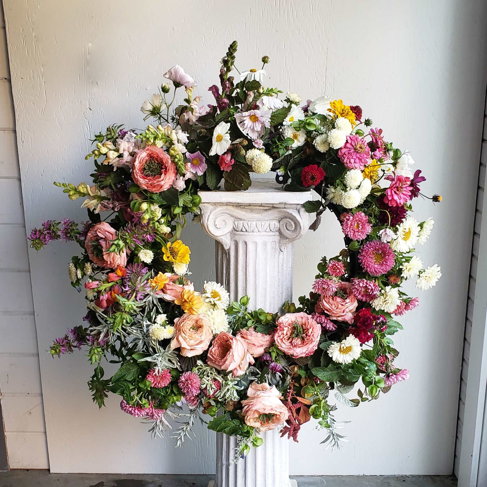 Large floral wreath with pink, white, and yellow blooms on a pedestal