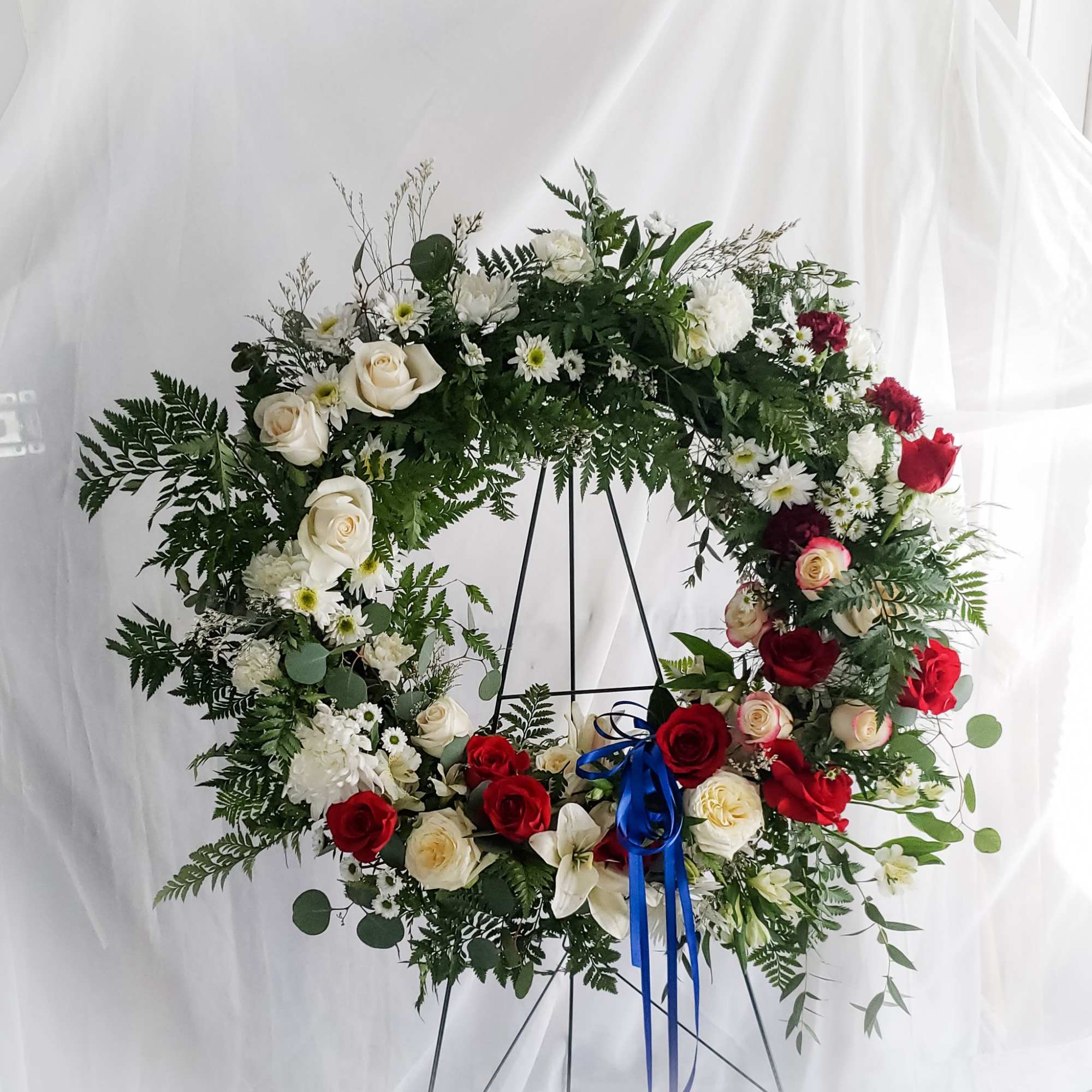 Circular floral wreath with red and white roses on a stand