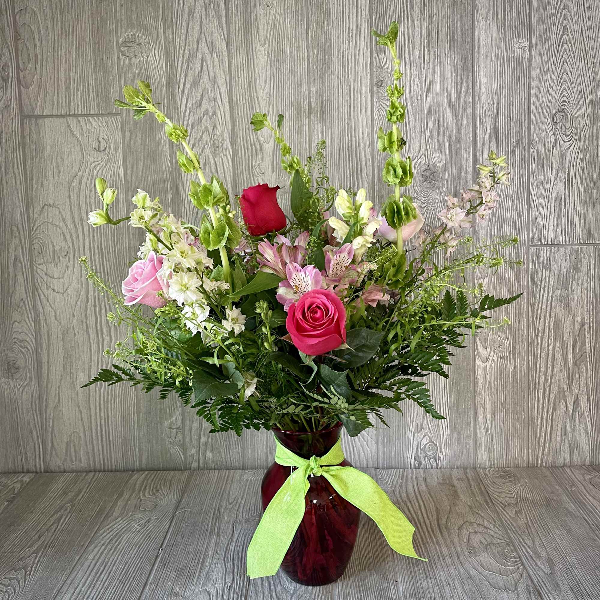 Mixed bouquet of pink and white flowers in a red glass vase with a green ribbon