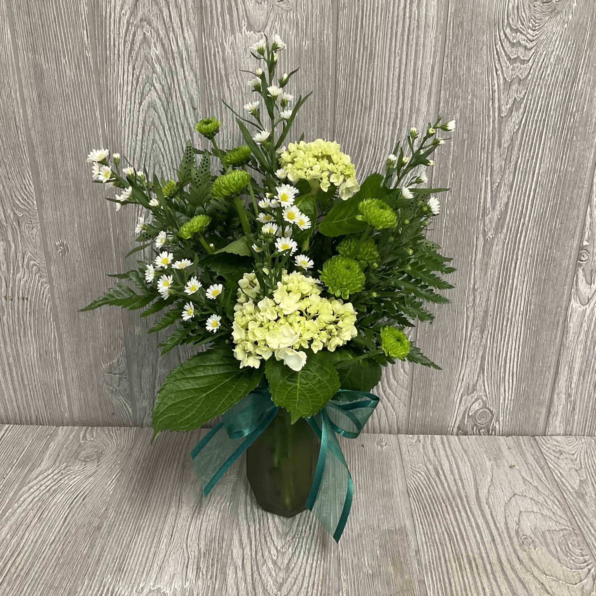 Green and white floral arrangement in a vase with a teal ribbon