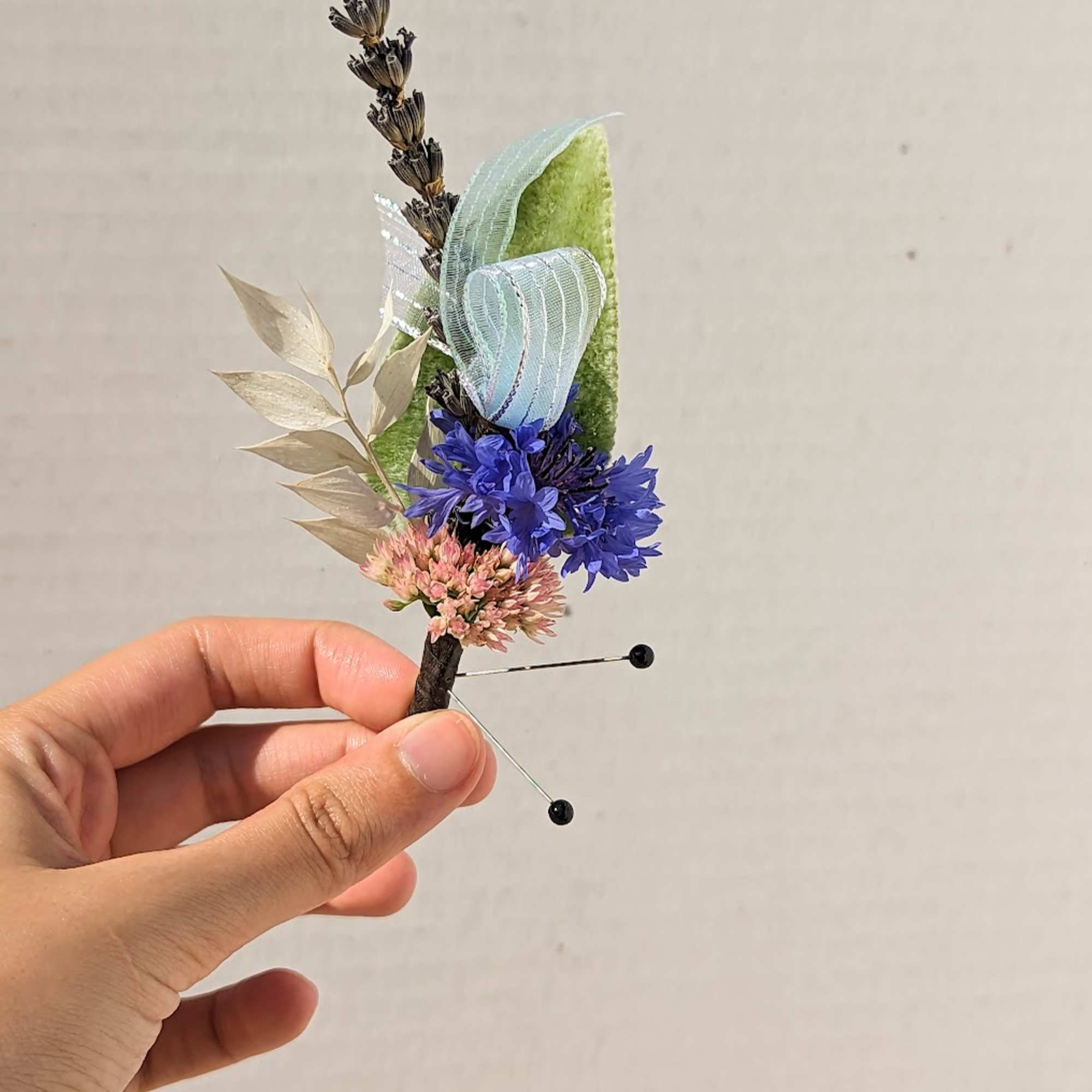 Small floral boutonniere with blue and pink flowers and ribbon