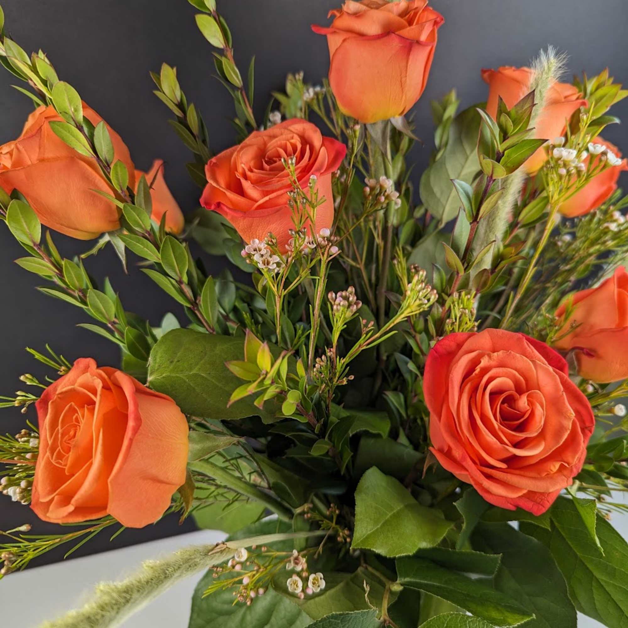 Bouquet of orange roses with mixed greenery in a vase