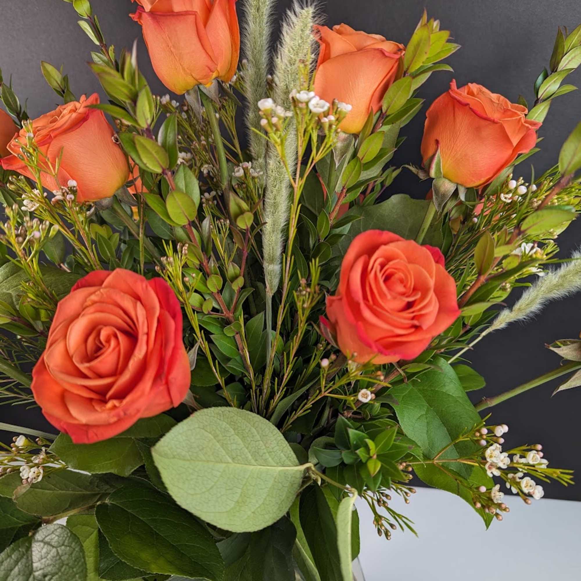 Orange roses in a clear glass vase with mixed greenery