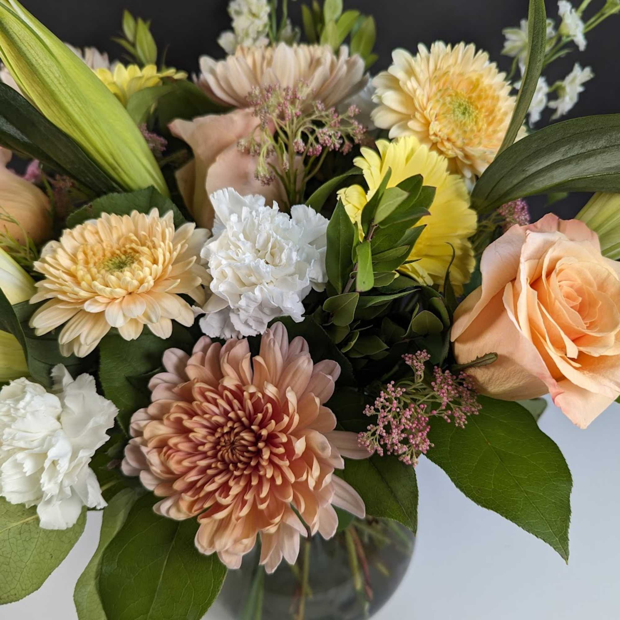 Mixed bouquet of peach, yellow, and white flowers in a glass vase