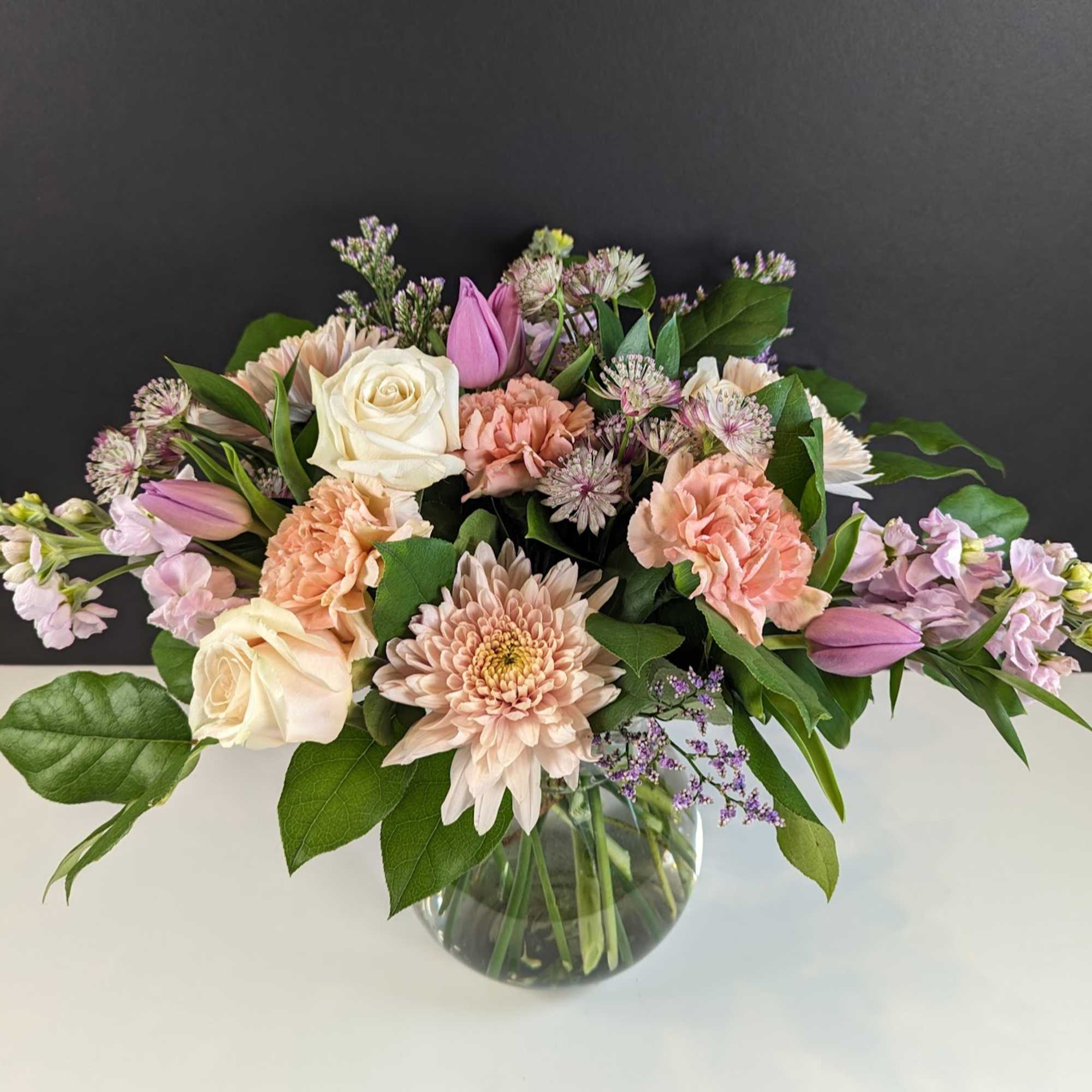 Pastel bouquet of roses, carnations, and chrysanthemums in a clear glass vase