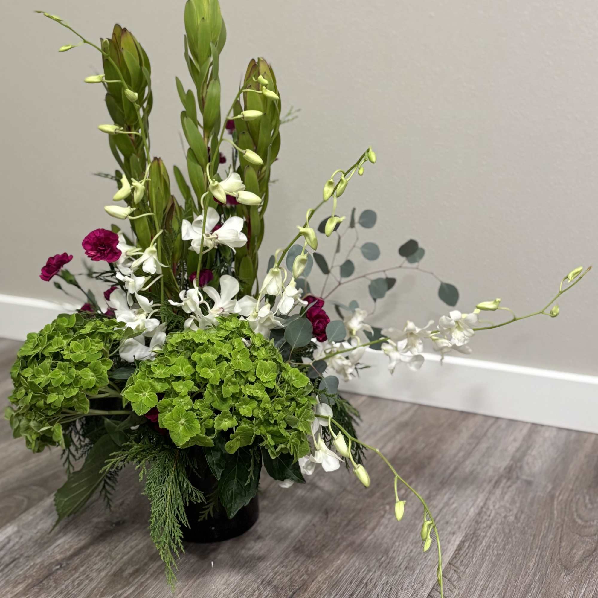 Tall floral arrangement with green hydrangeas, white orchids, and magenta blooms in a black vase