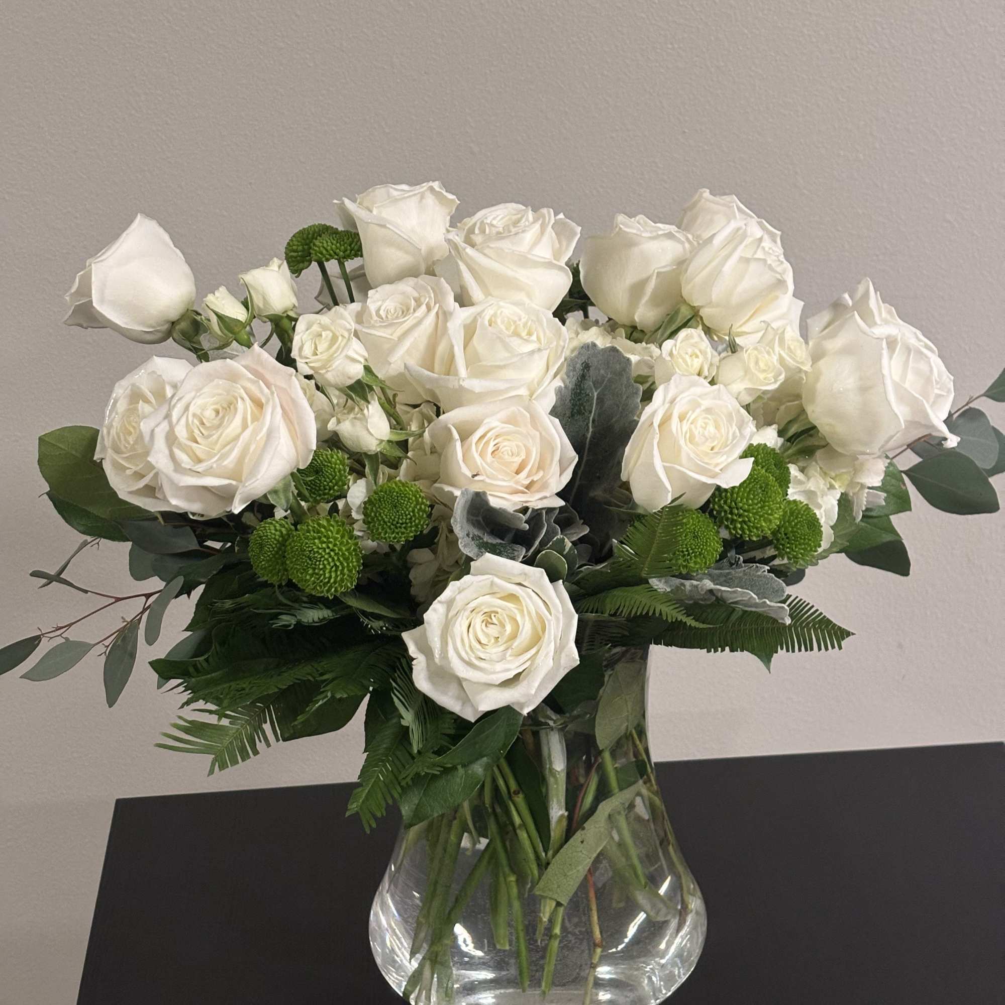 White rose bouquet in a clear glass vase with green accents