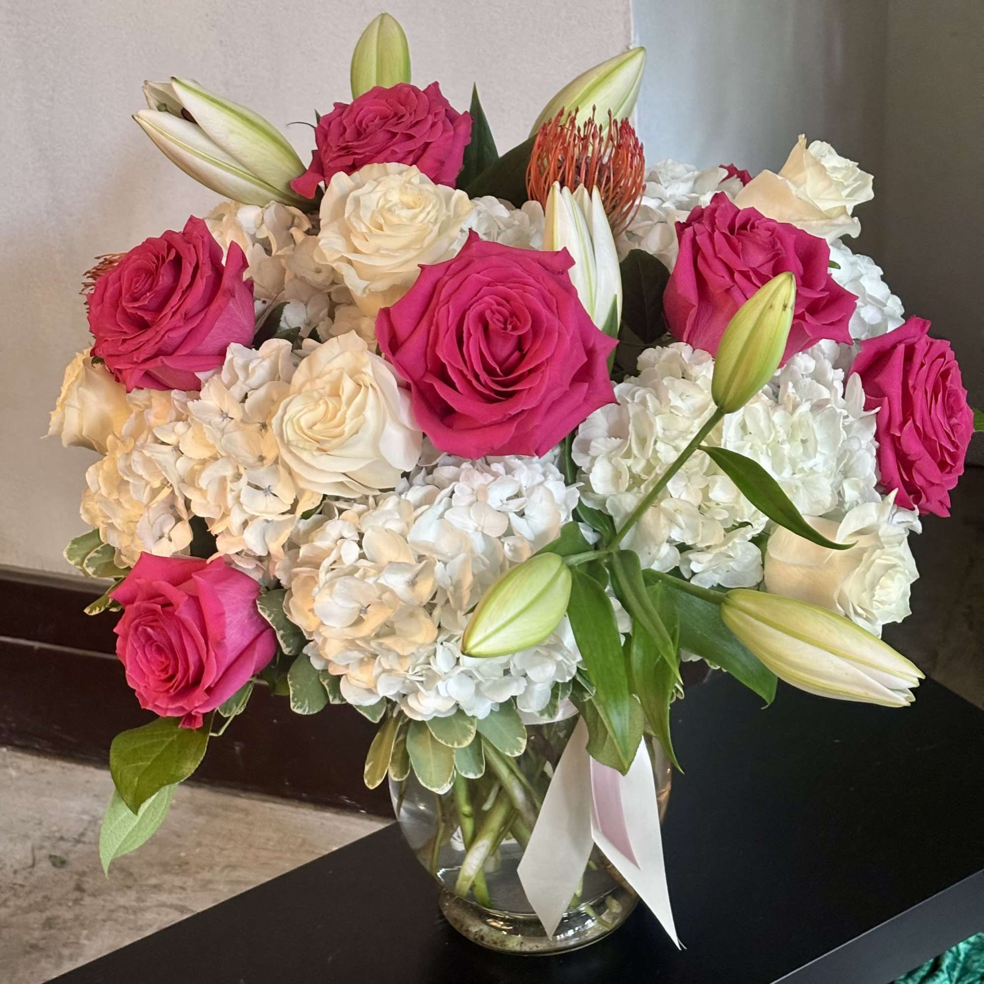 Bouquet of hot pink roses, white hydrangeas, and lilies in a glass vase