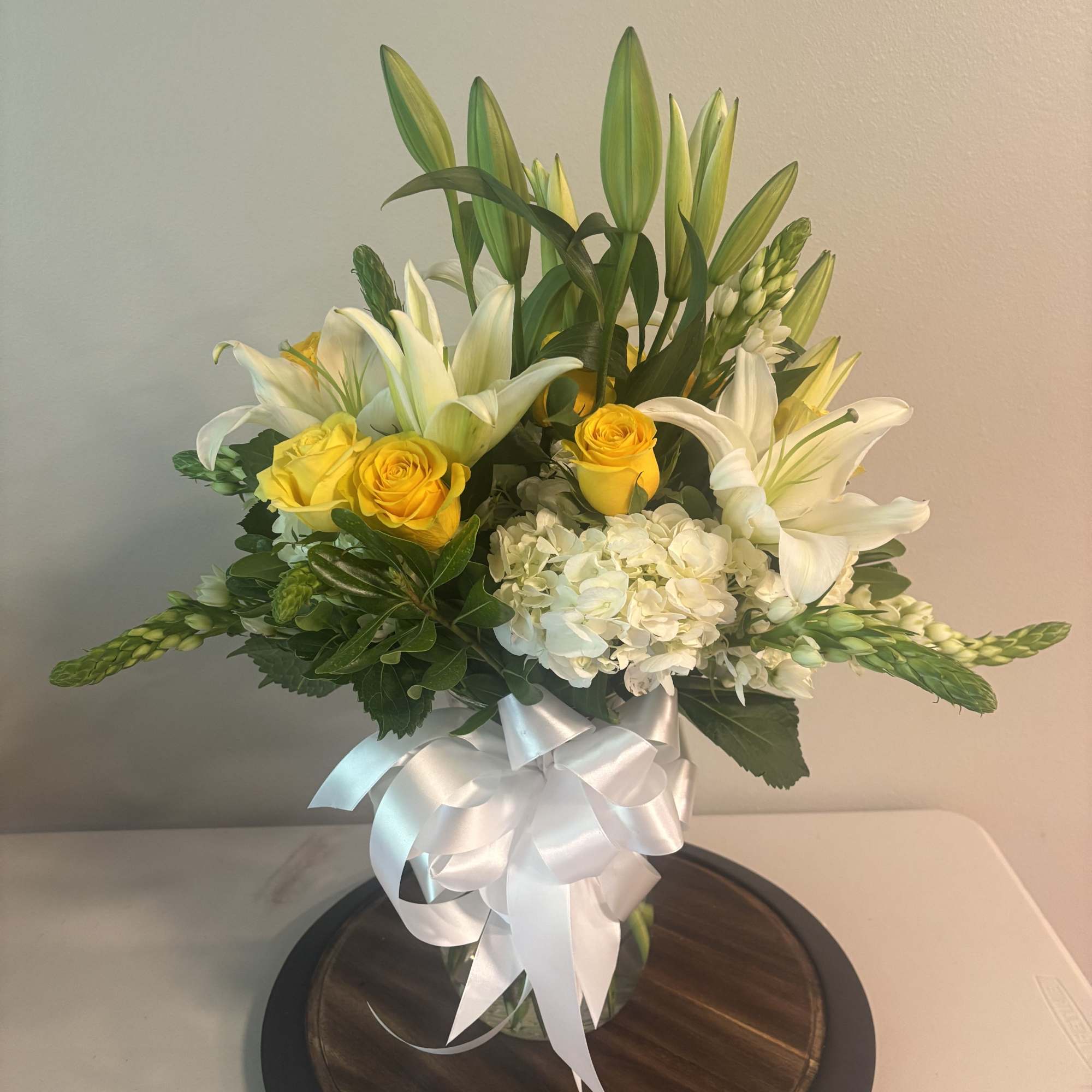 Bouquet of white lilies, yellow roses, and white hydrangeas in a glass vase with a white ribbon
