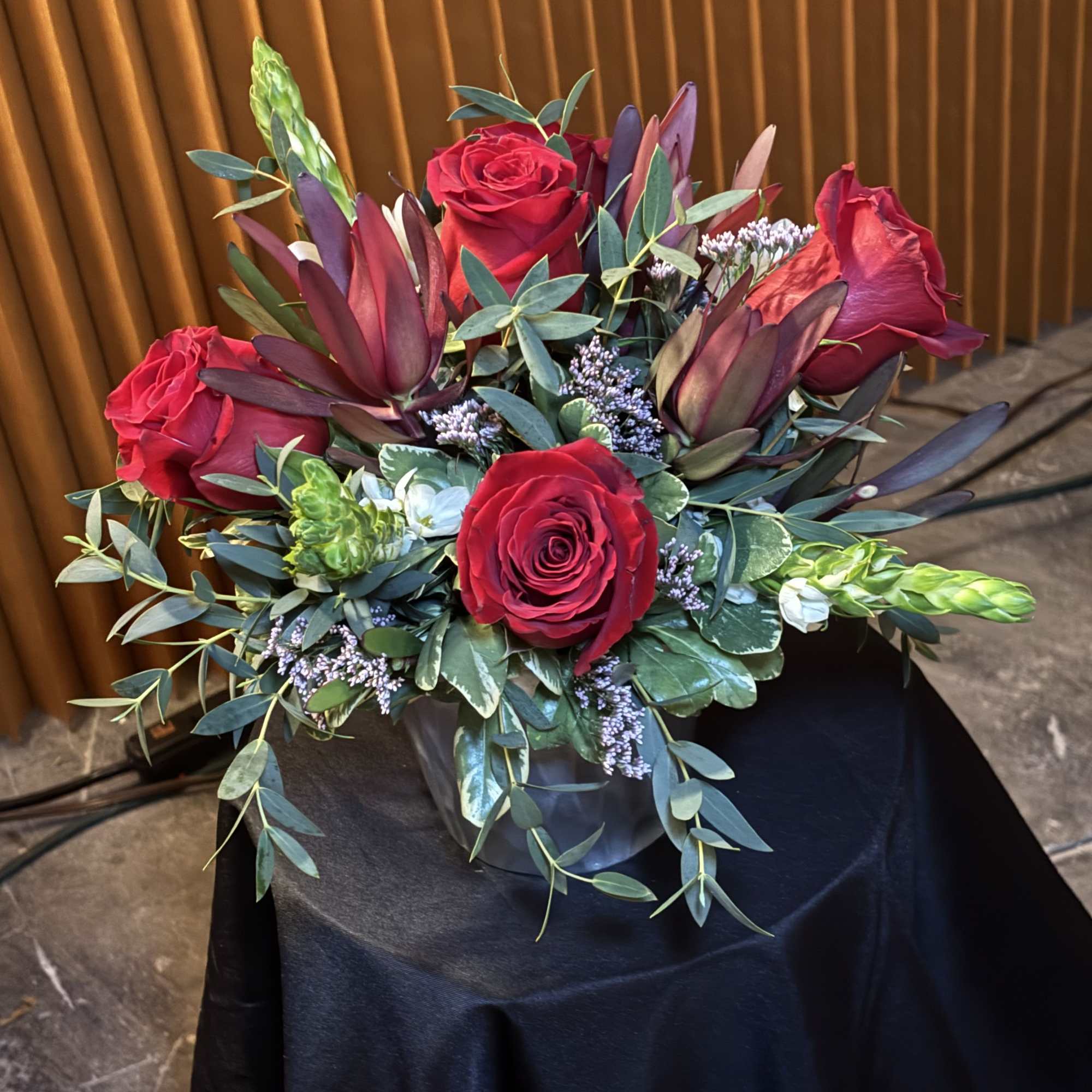 Red roses and burgundy flowers arranged in a low vase