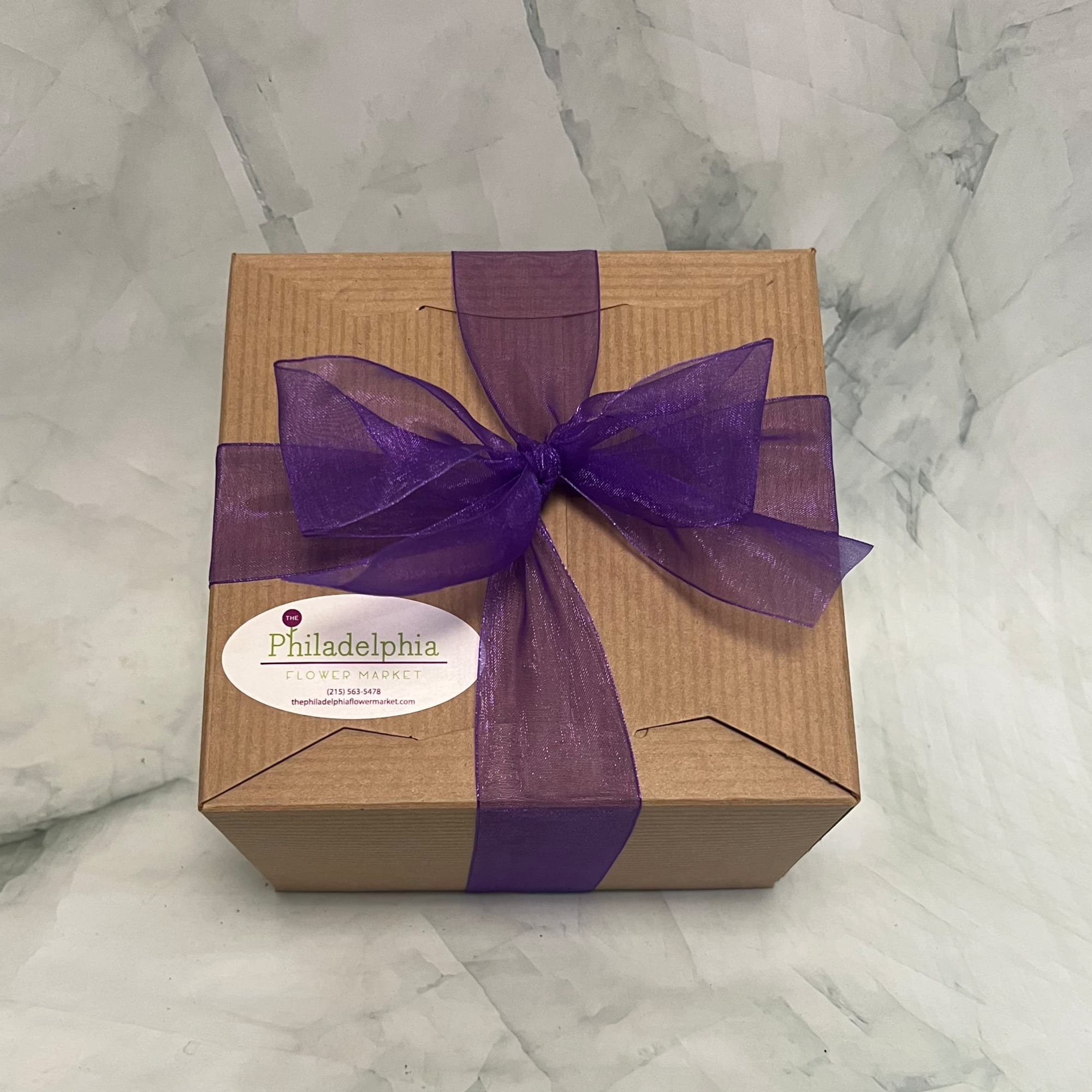 Brown gift box tied with a purple ribbon and bow