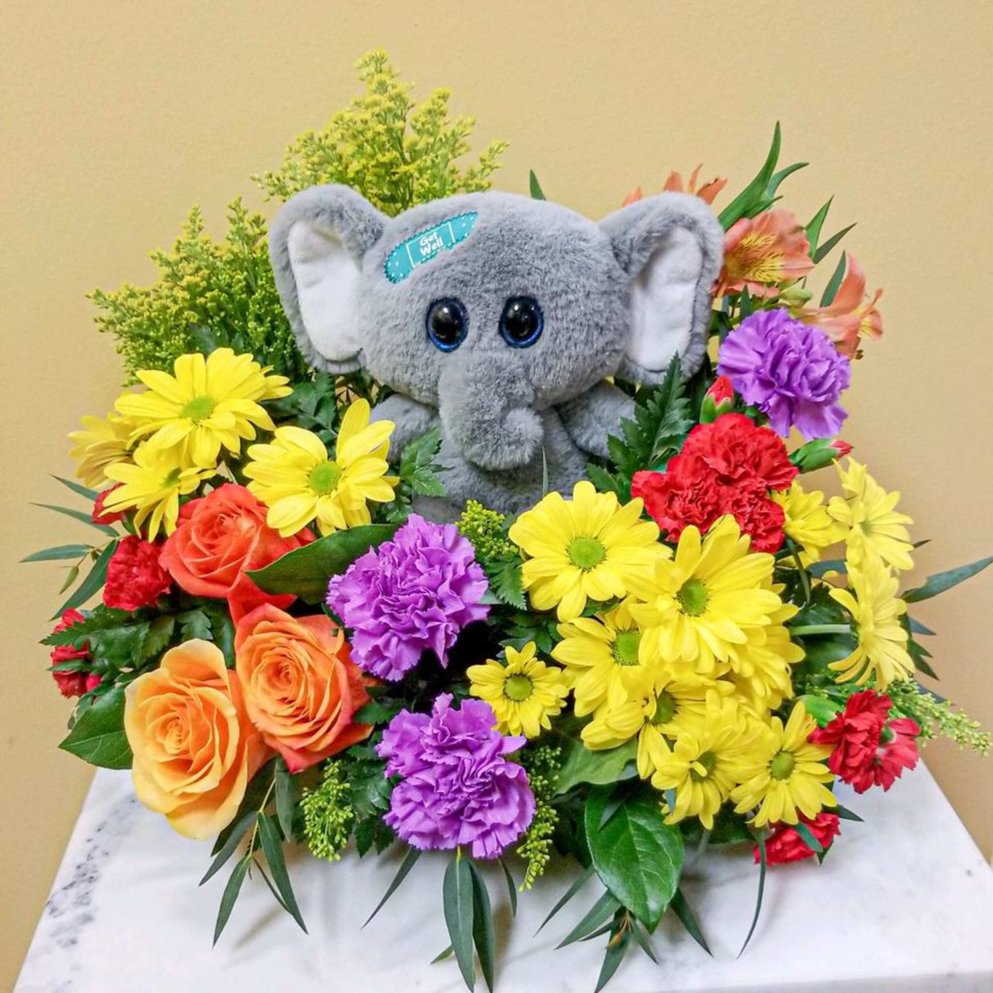 Plush gray elephant surrounded by colorful flowers in a gift arrangement