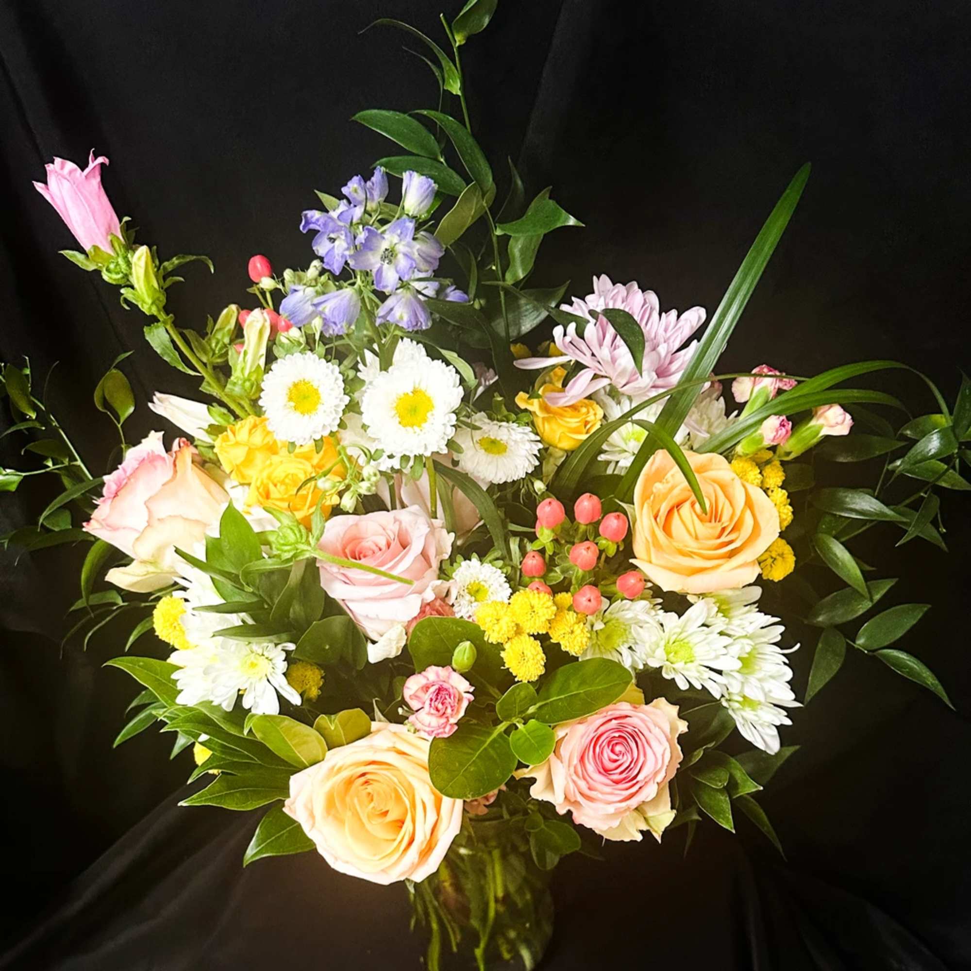 Mixed bouquet of roses, daisies, and purple blooms in a glass vase