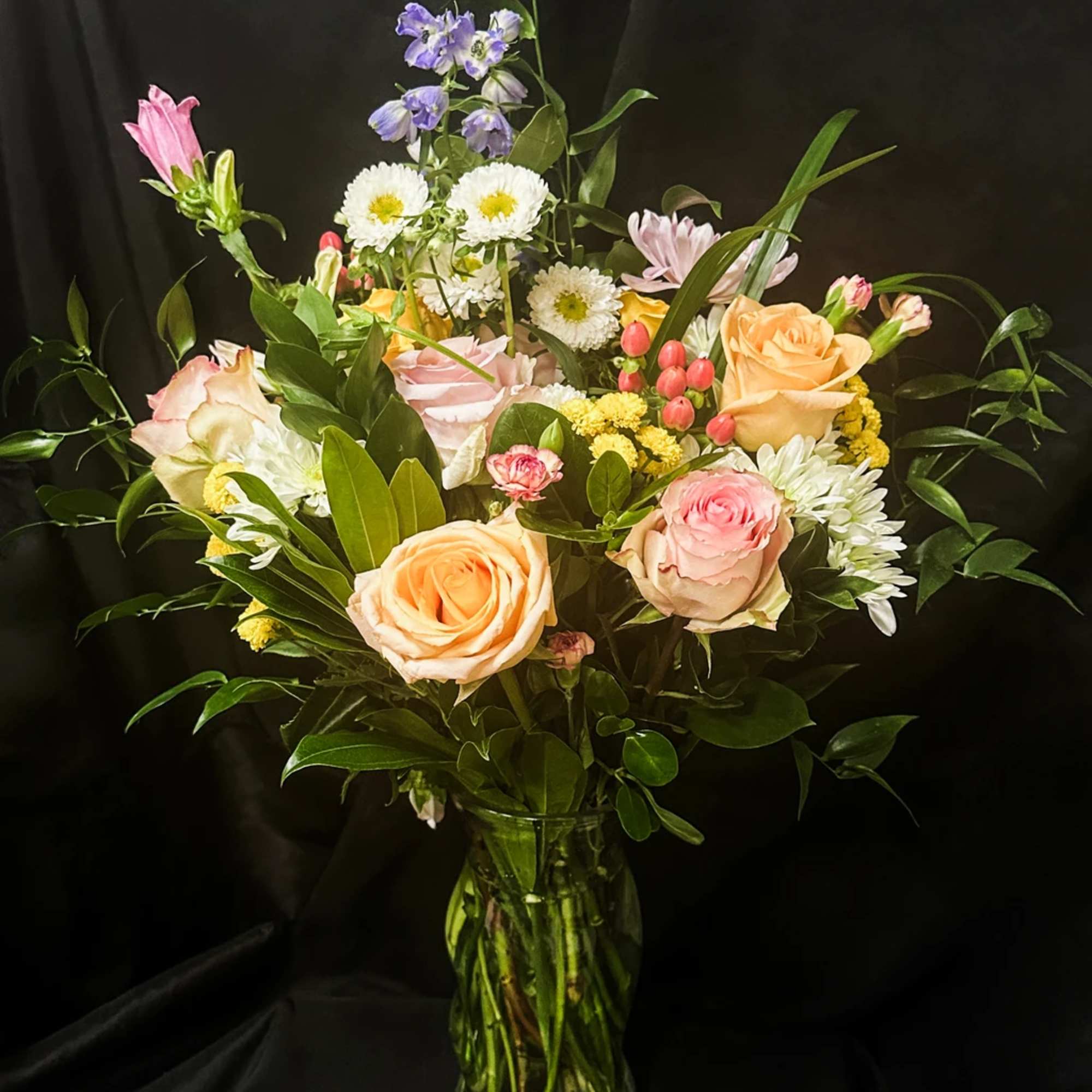 Mixed bouquet of roses, daisies, and purple flowers in a glass vase