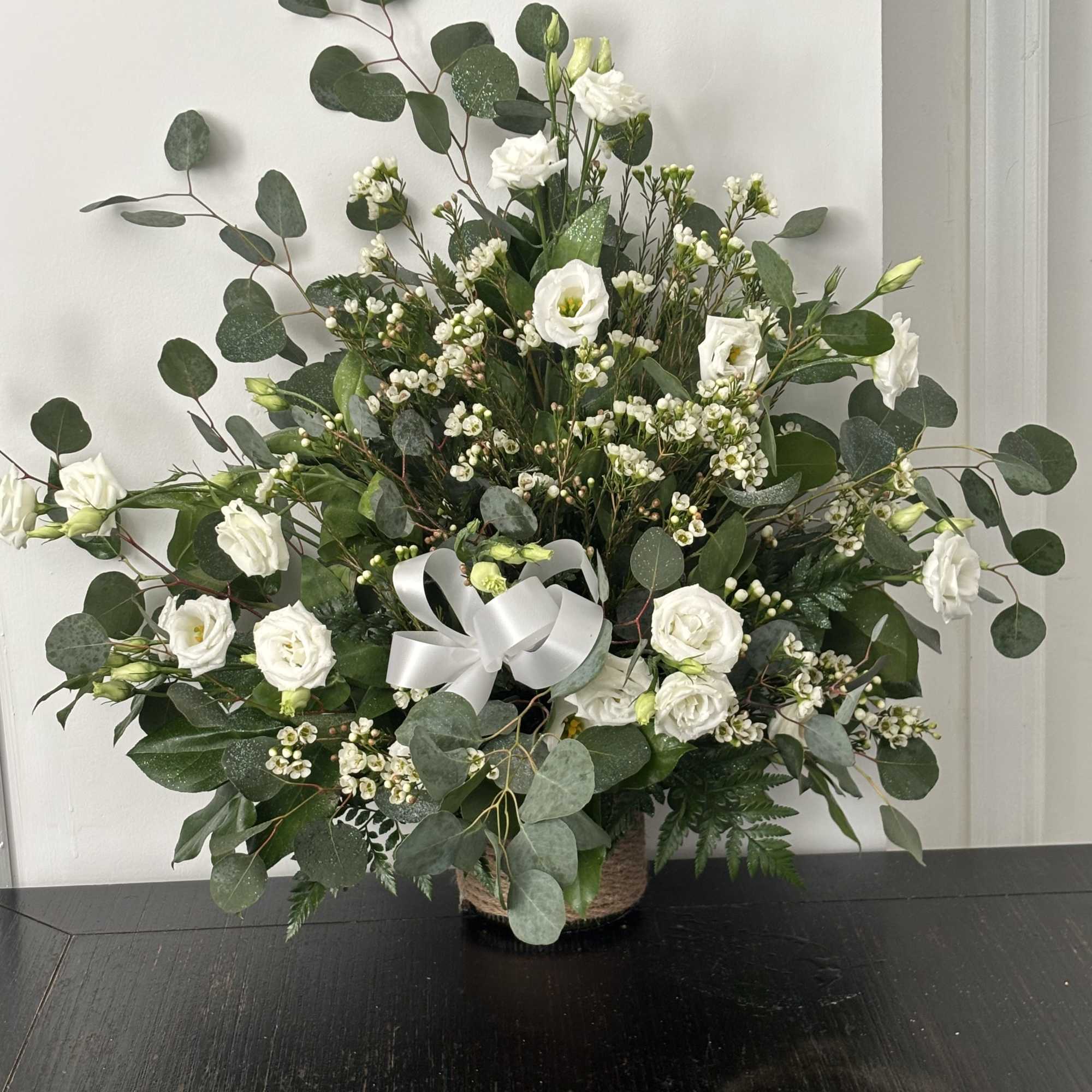 White flowers in a basket with eucalyptus and a white ribbon