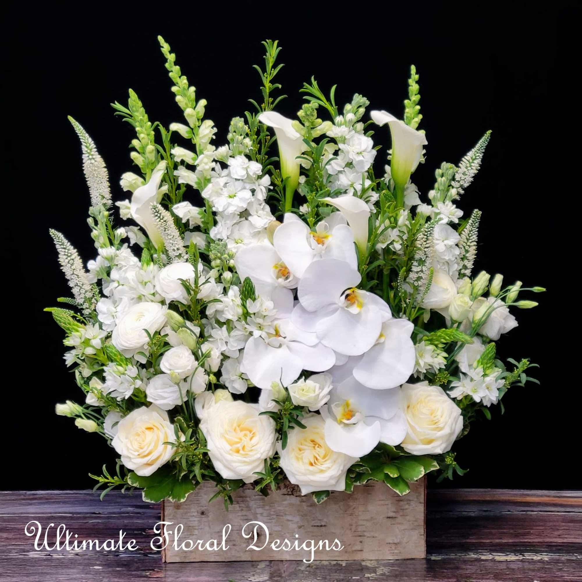 White floral arrangement with orchids, roses, and calla lilies in a wooden box