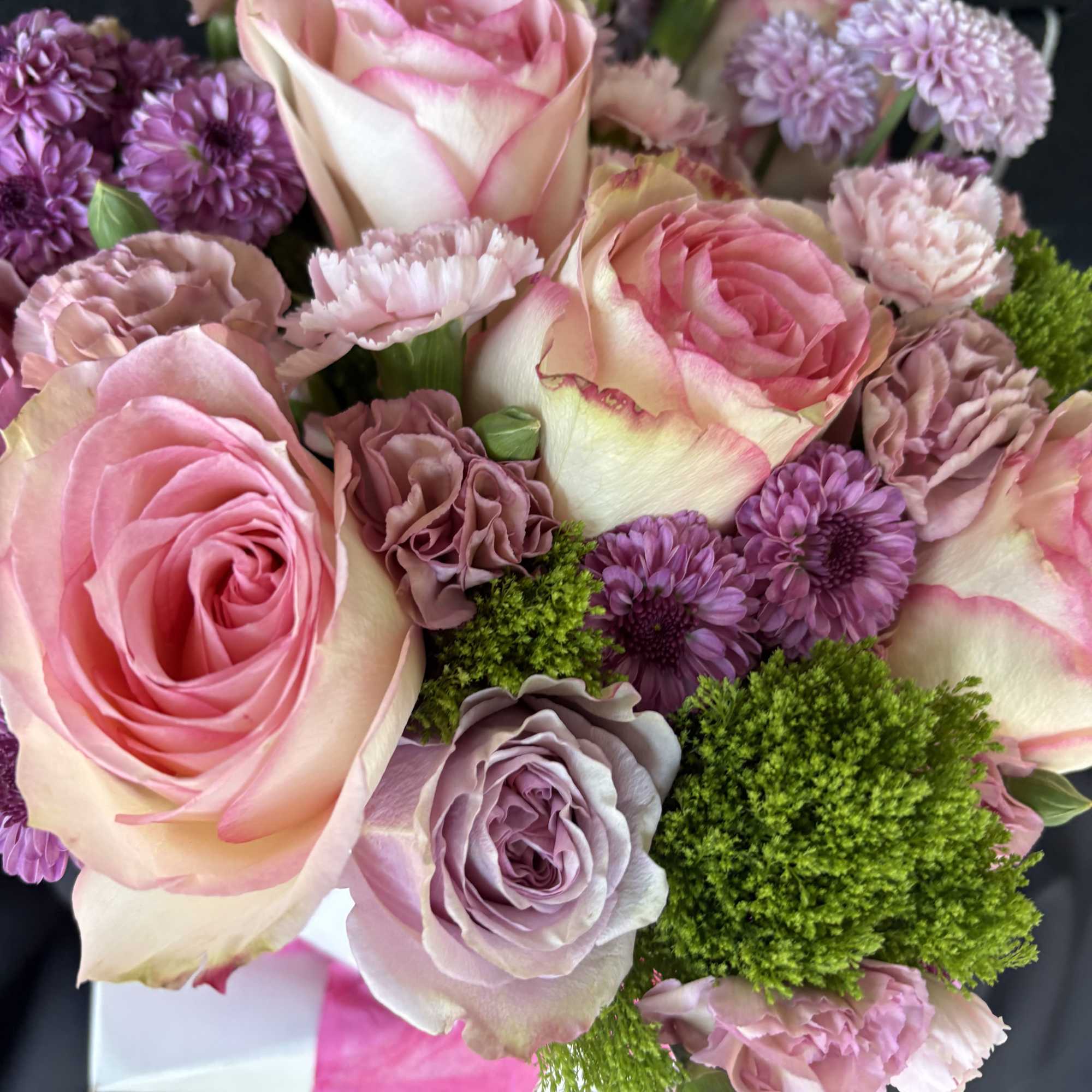 This arrangement has greenery, different types of season, flowers, pink and purple