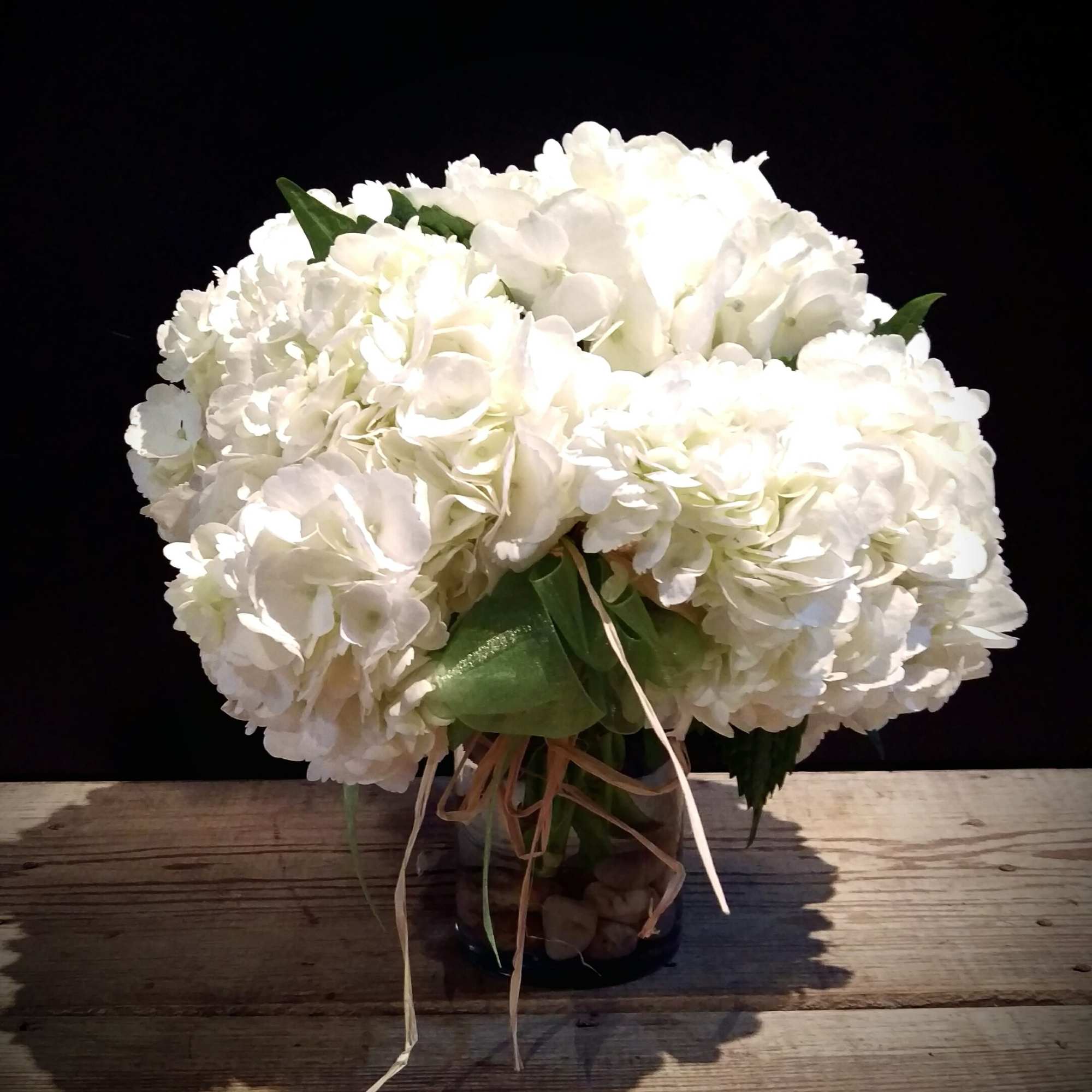 White hydrangea bouquet tied with ribbon in a glass vase
