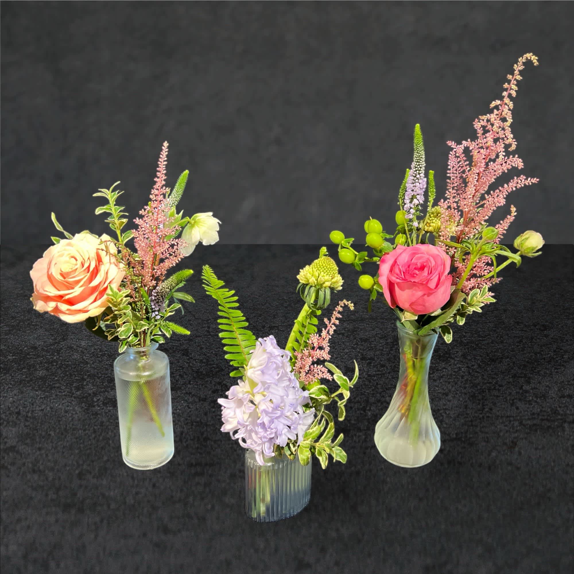 Three small floral arrangements in glass vases with roses and pastel blooms