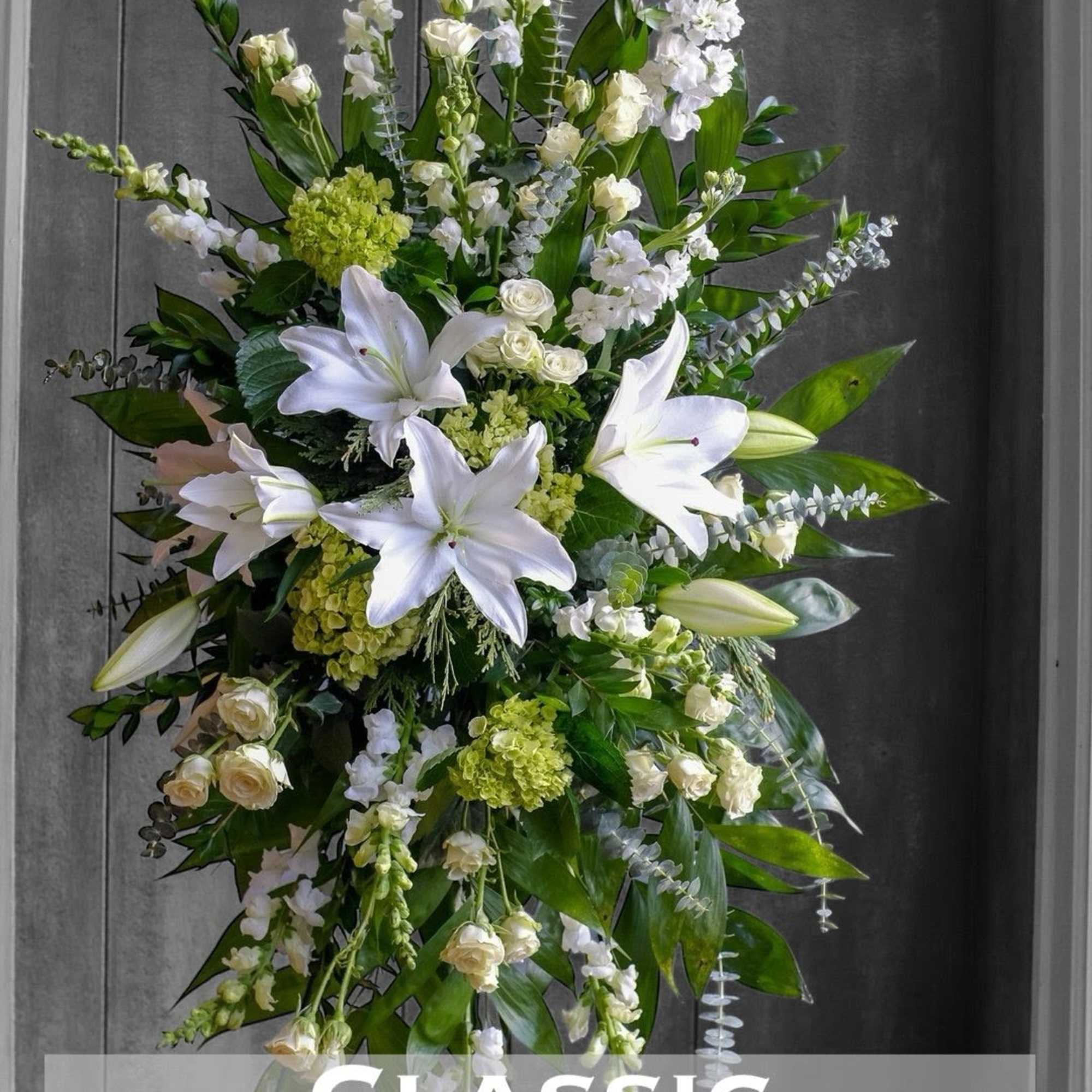 White lilies and mixed white flowers in a standing spray with green foliage