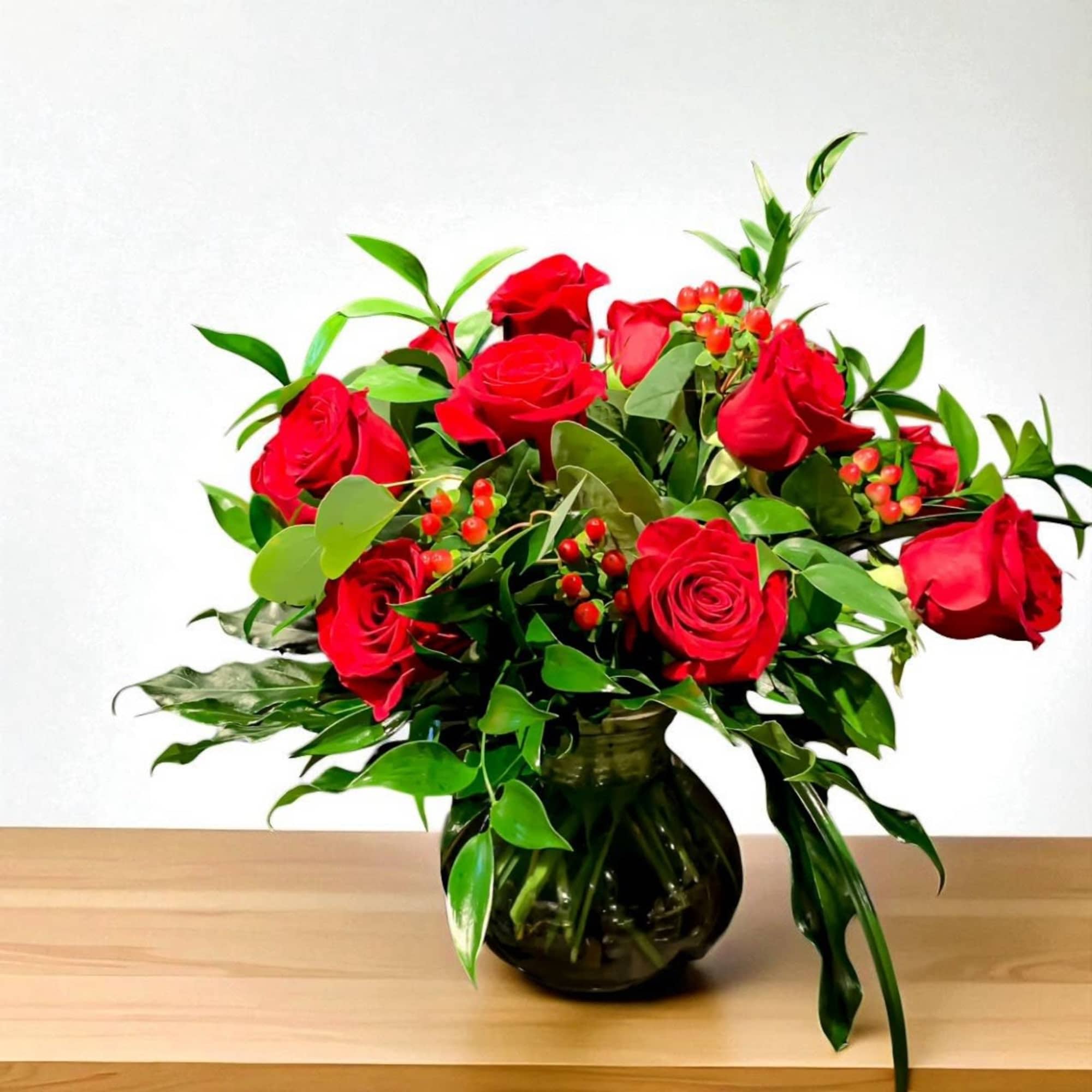 Red roses arranged in a dark glass vase with green foliage