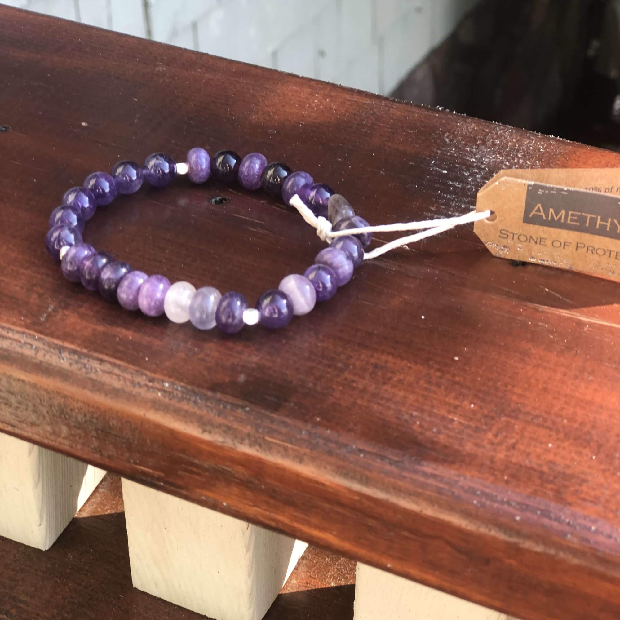 Purple beaded bracelet on a wooden shelf with a paper tag