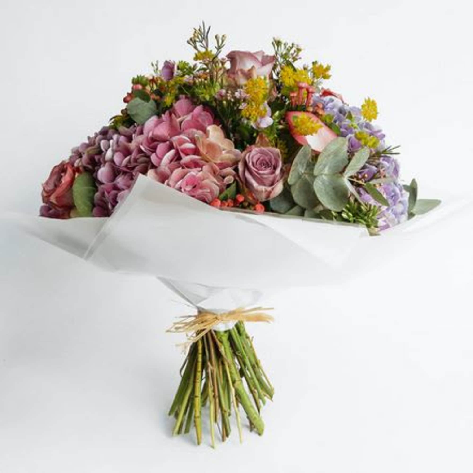 Mixed bouquet of pink, purple, and yellow flowers wrapped in white paper