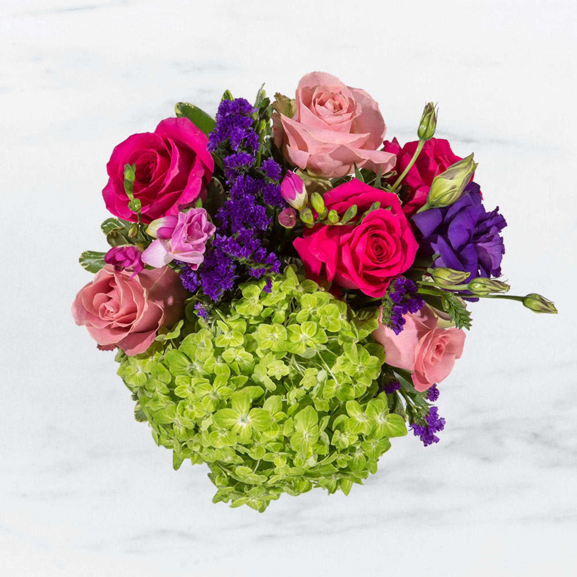 This arrangement includes hot pink roses, pink roses, green hydrangea, freesia, lisianthus