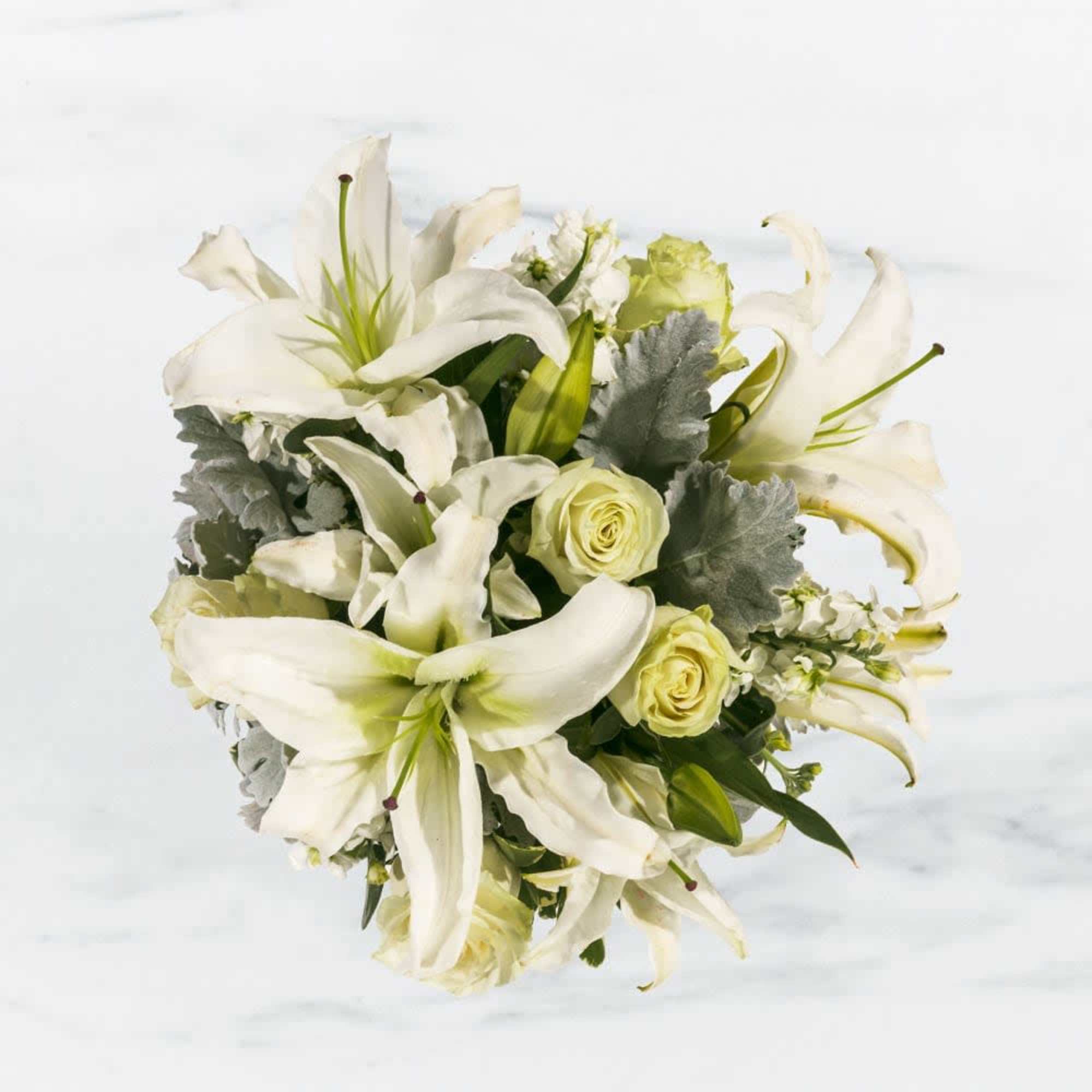 This arrangement includes white roses, white asiatic lilies, white stock, and dusty