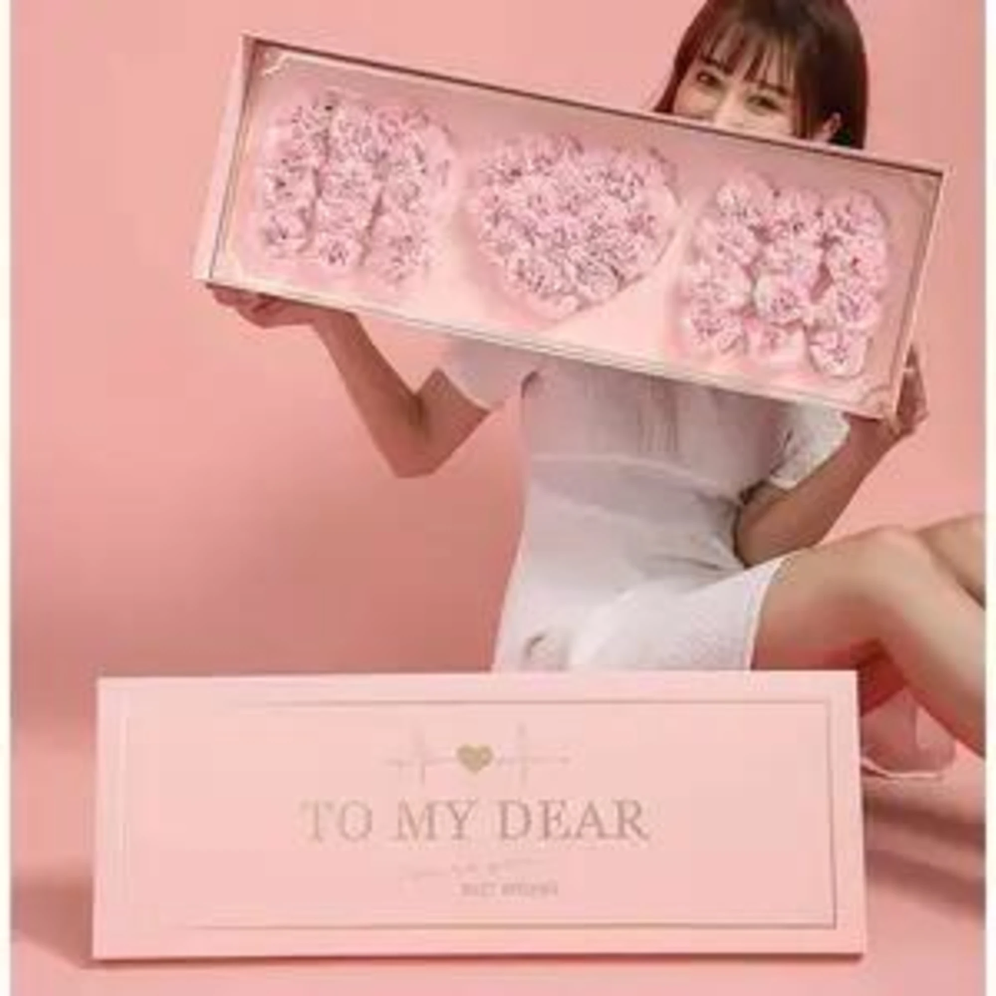Woman holding a pink gift box with three heart-shaped floral arrangements