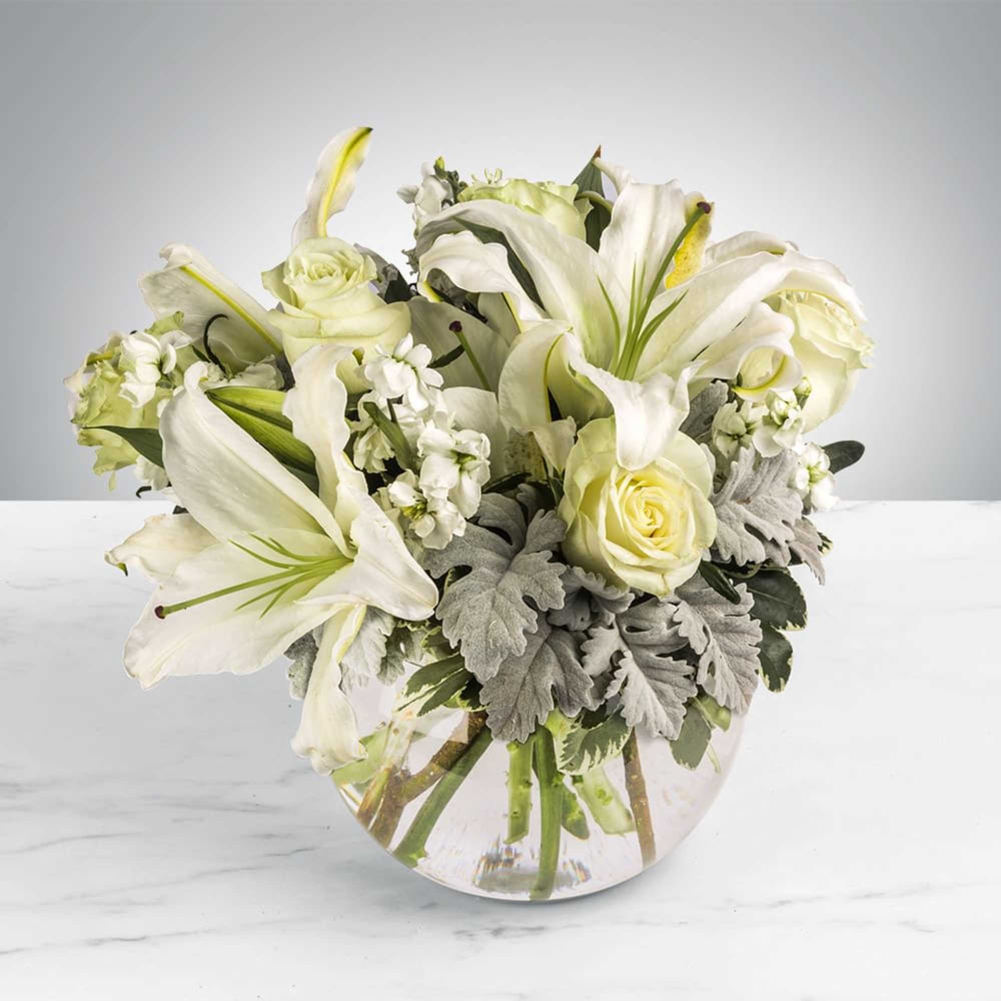 This arrangement includes white roses, white asiatic lilies, white stock, and dusty