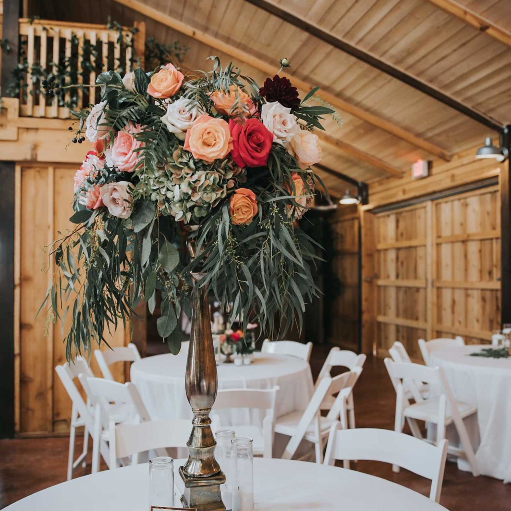 Tall floral centerpiece with roses and greenery in a metallic vase