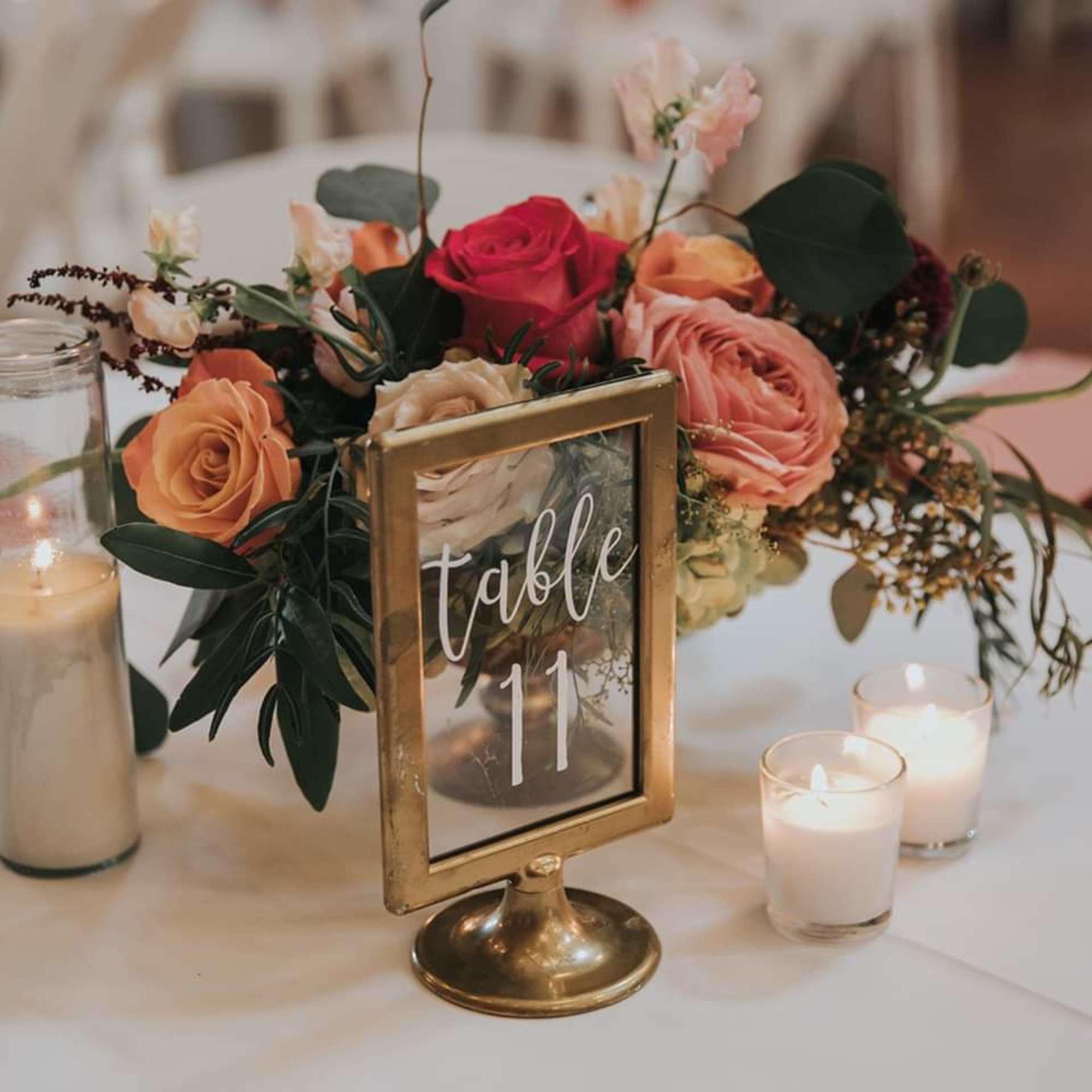 Floral table centerpiece with roses and candles beside a table number sign