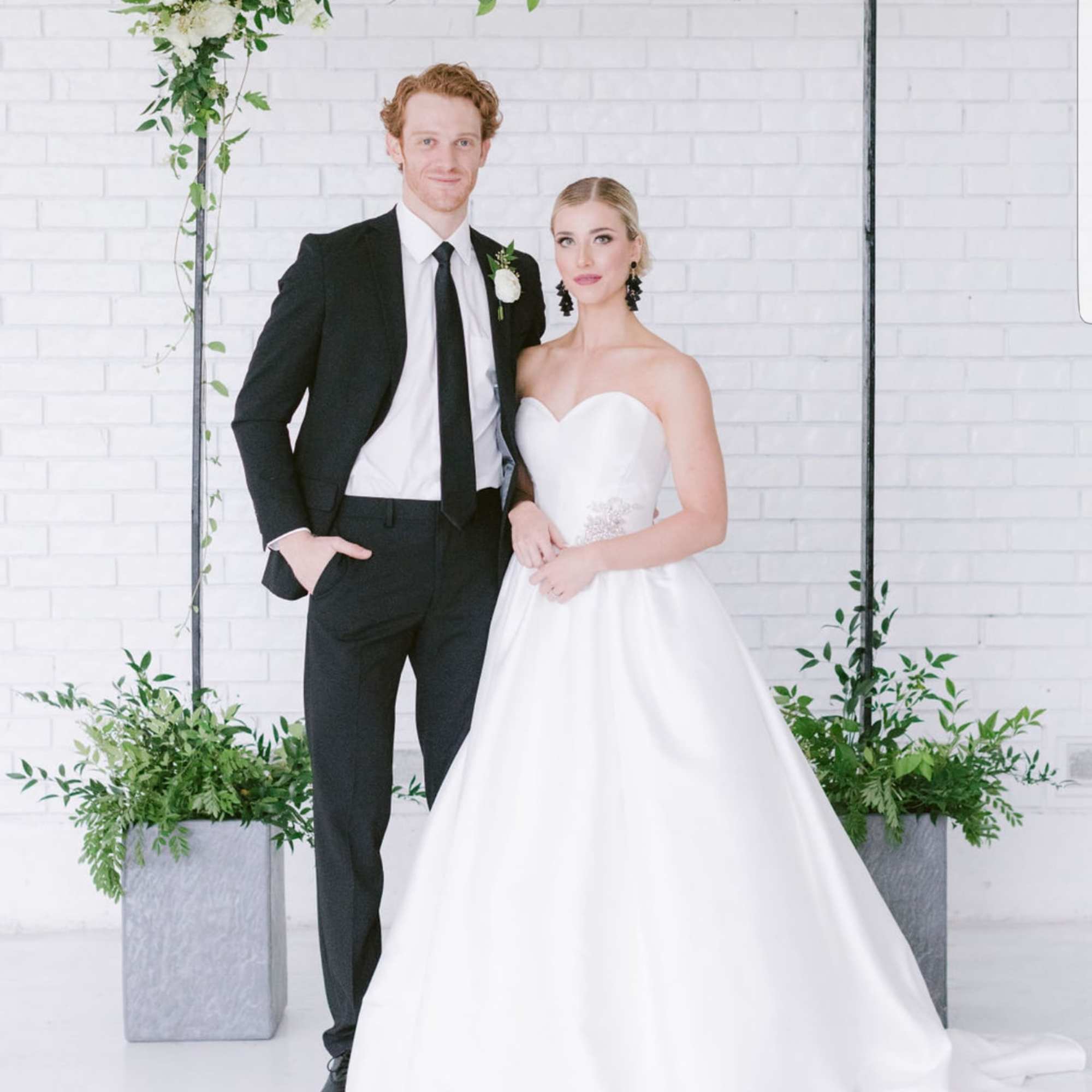 Bride and groom posing beside a white floral arch with greenery