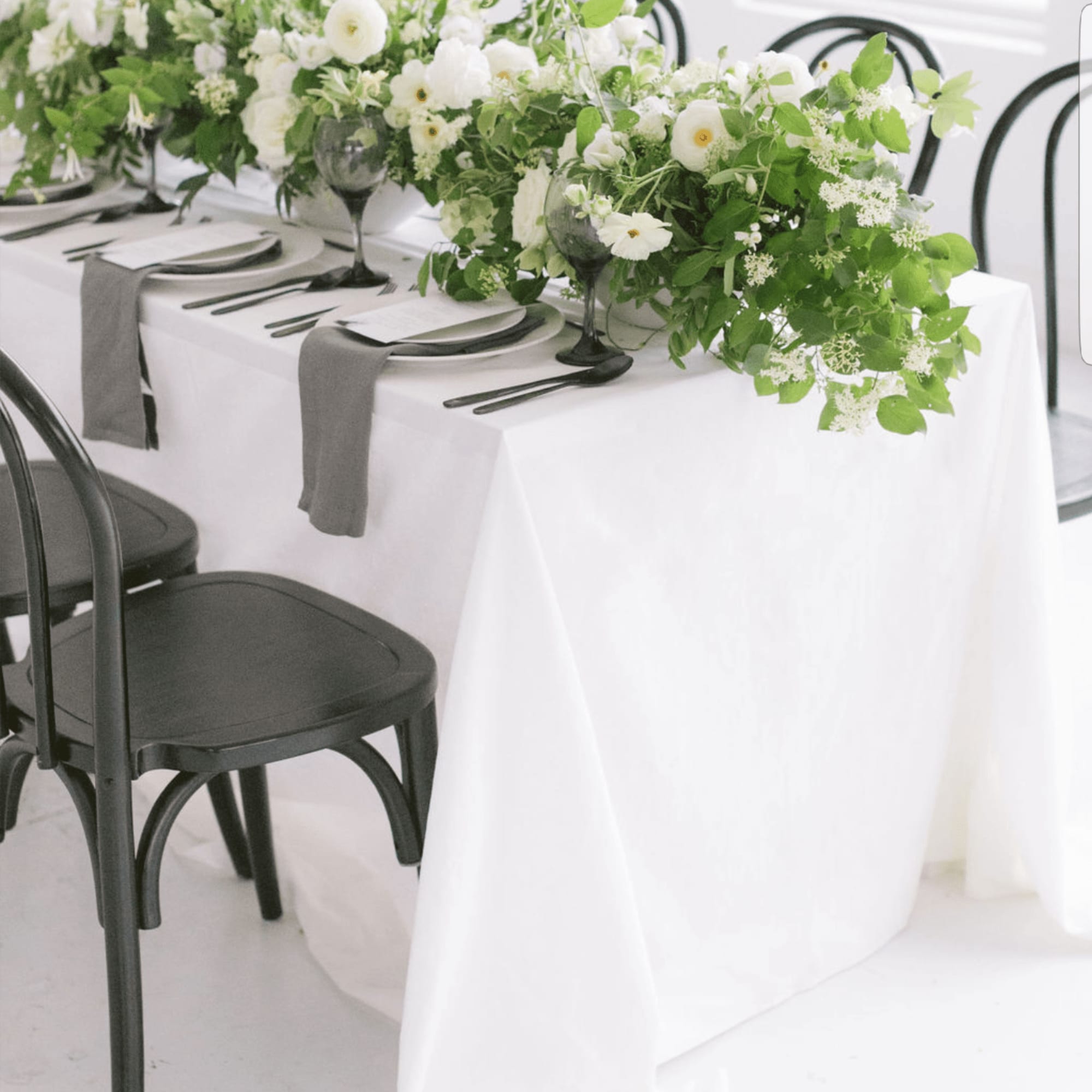 White floral centerpieces on a long table with black chairs