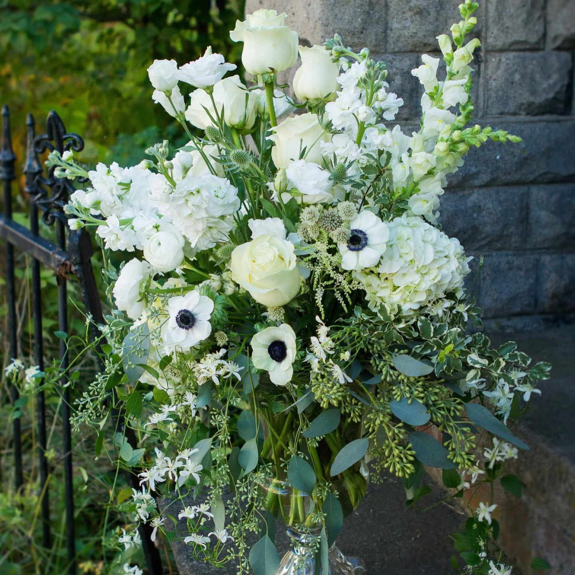 Tall white arrangement of roses, hydrangeas, anemones and snapdragons in a clear glass vase