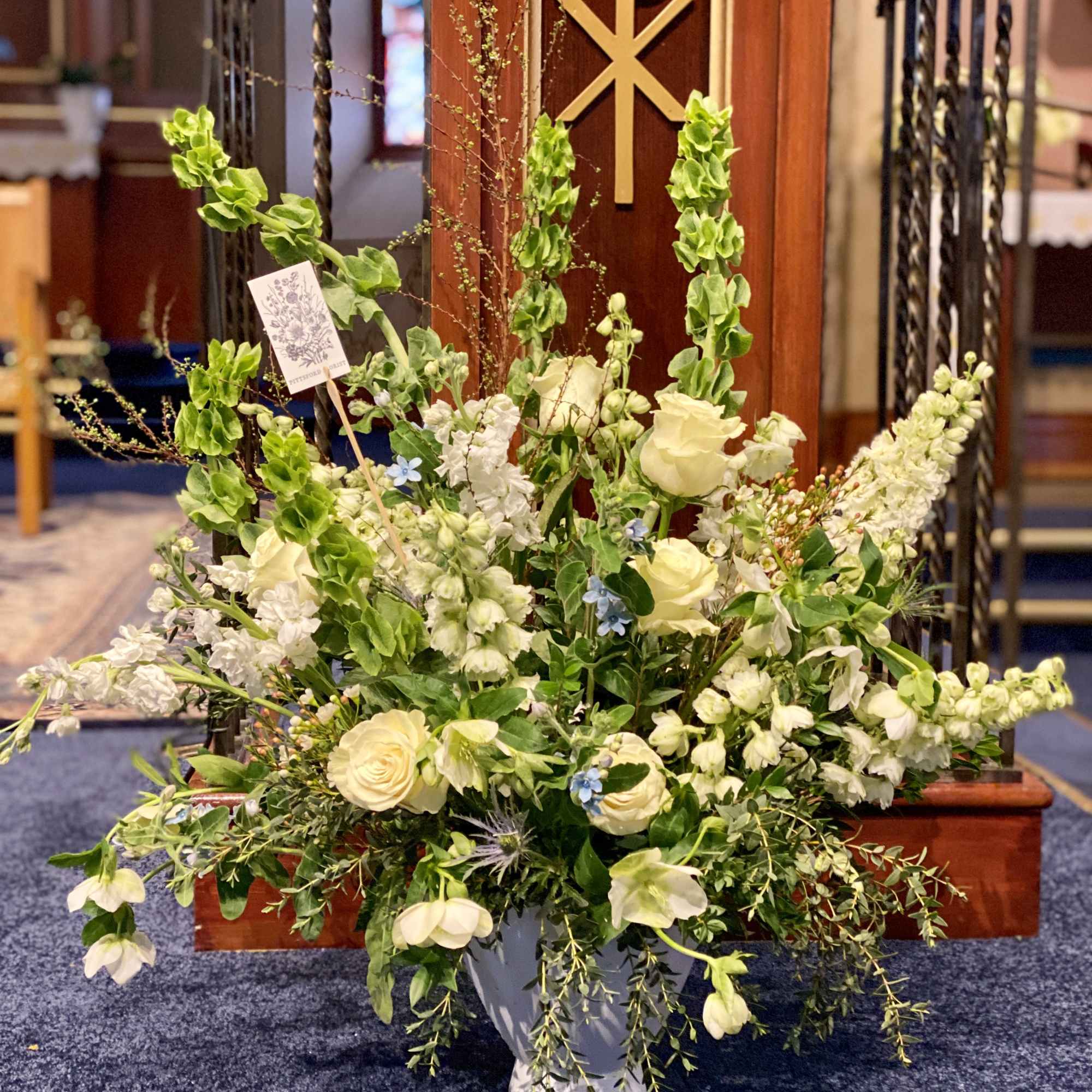 Large white and cream arrangement with roses and bells of Ireland in a white urn in a church.