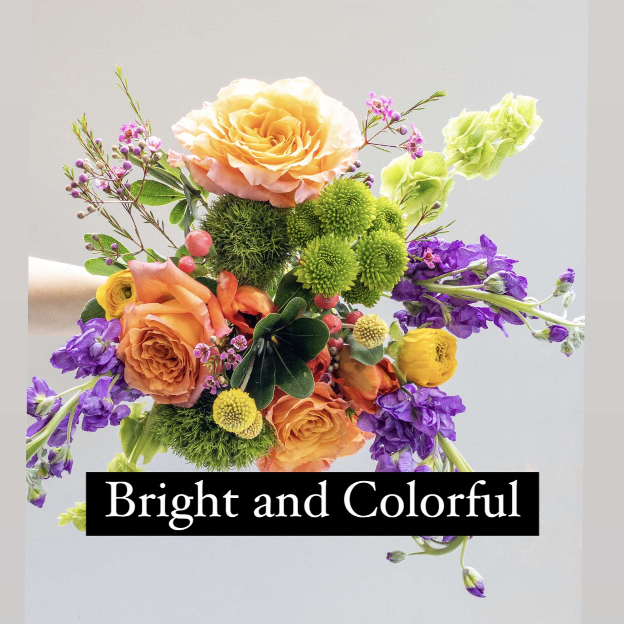 Hand-tied bouquet of orange roses with yellow, green, and purple mixed flowers on a light background