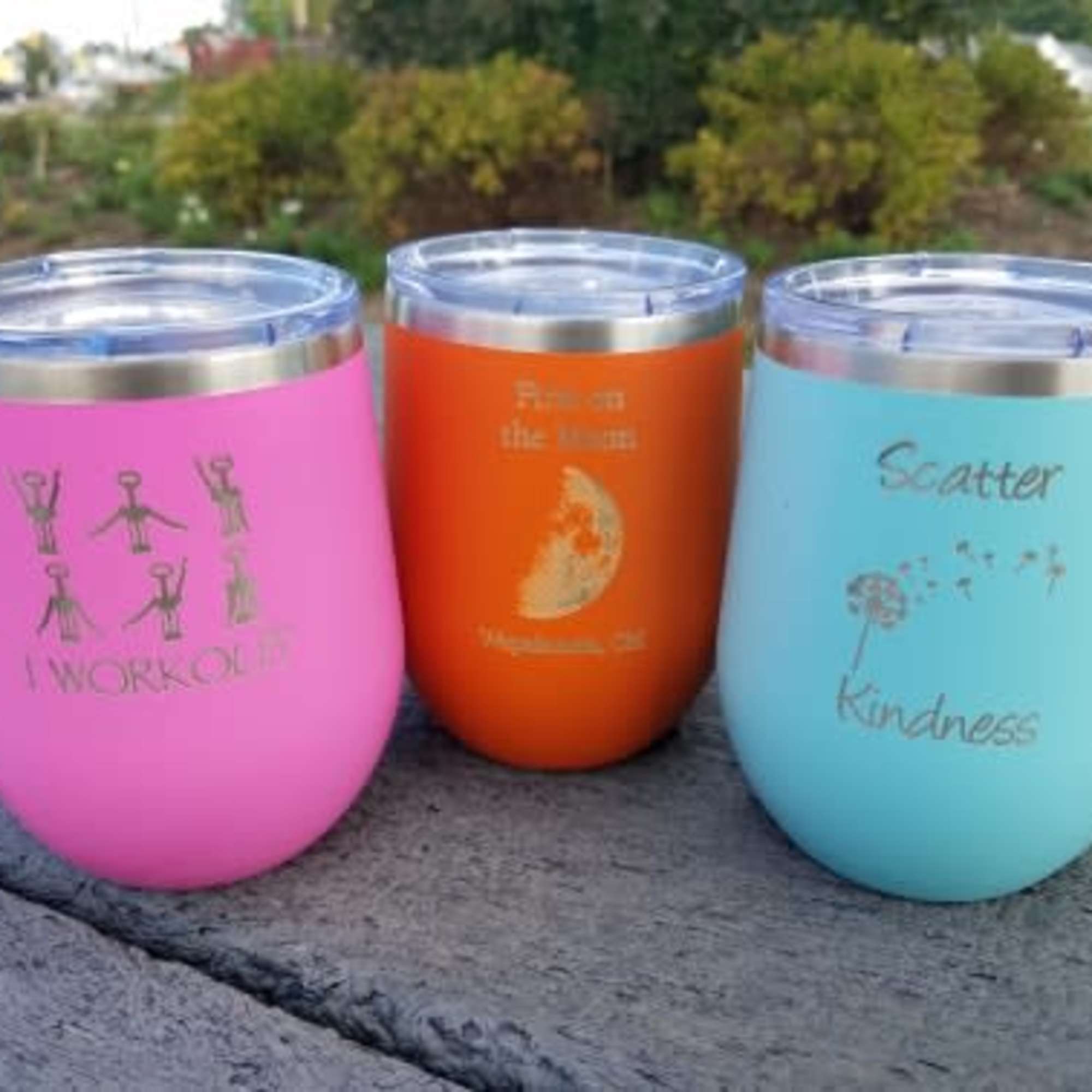 Three colorful insulated tumblers with printed sayings on a stone surface