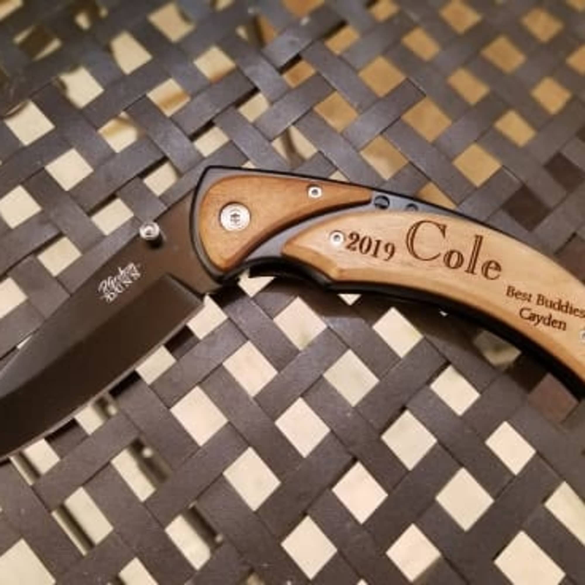 Engraved folding knife with a wooden handle on a woven surface