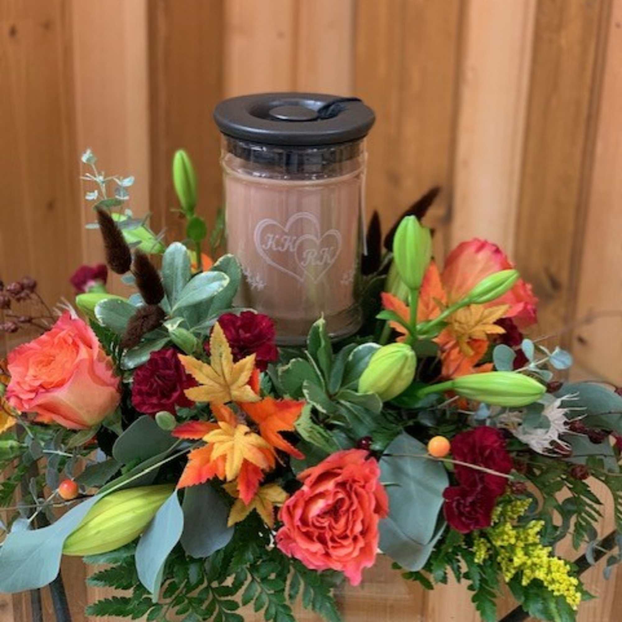 Floral arrangement around a lidded candle jar with roses and lilies