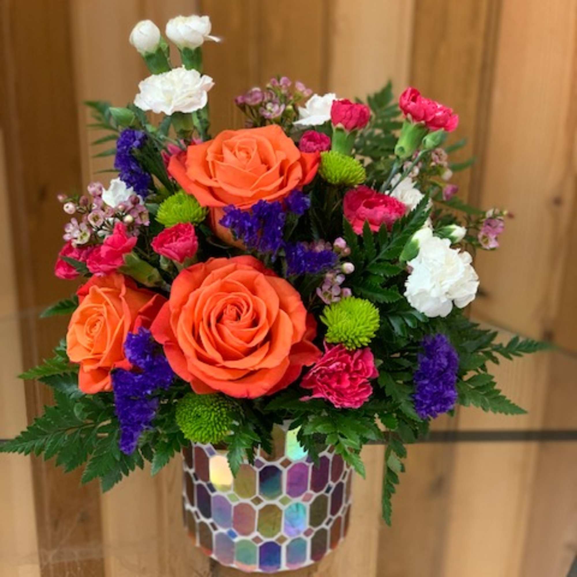 Orange and white roses with pink and purple accents in a mosaic vase